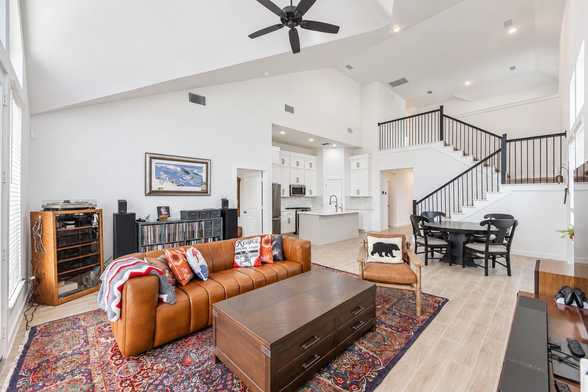 16922 Warm Glow Court, Hockley, TX 77447 Spacious open-concept living area featuring a vaulted ceiling, elegant staircase, and a modern kitchen with a large island. Natural light floods through expansive windows, highlighting the stylish decor and inviting atmosphere.
