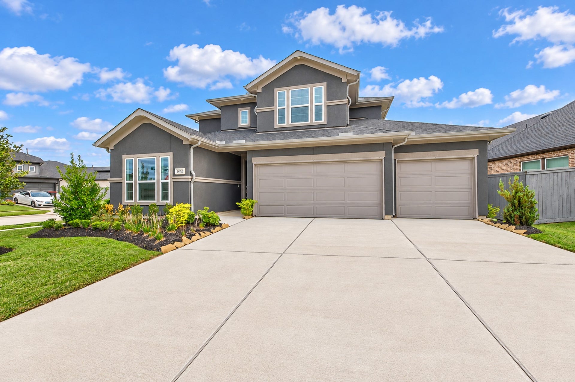 16922 Warm Glow Court, Hockley, TX 77447 Stunning modern home with a spacious three-car garage, manicured landscaping, and a sleek gray exterior, perfect for family living.
