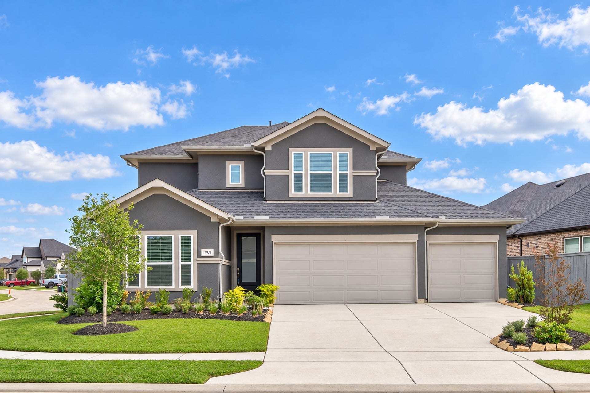 16922 Warm Glow Court, Hockley, TX 77447 Stunning two-story home with a modern gray facade, three-car garage, and beautifully landscaped front yard on a corner lot.