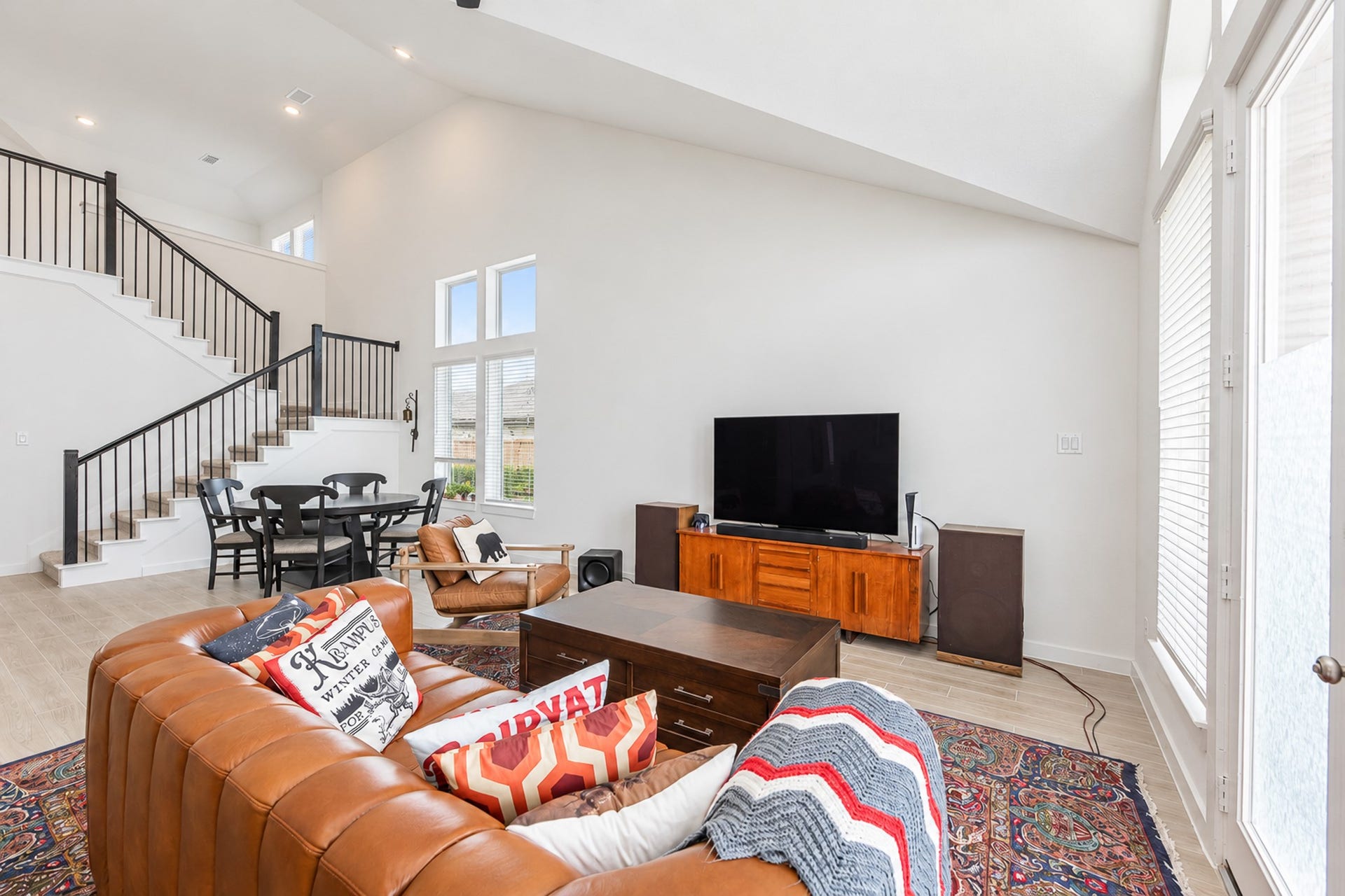 16922 Warm Glow Court, Hockley, TX 77447 Spacious living area with high ceilings, featuring a cozy leather sofa, a large TV, and natural light from tall windows. The open staircase leads to a charming dining nook, enhancing the inviting atmosphere.