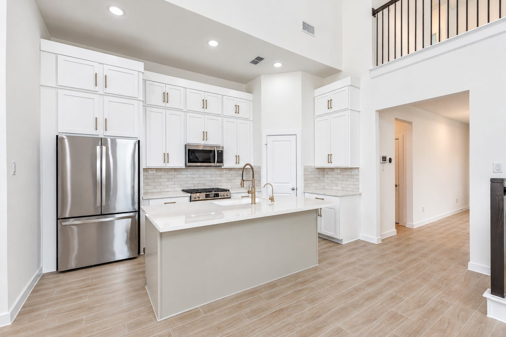 16922 Warm Glow Court, Hockley, TX 77447 Elegant kitchen with high ceilings, modern stainless steel appliances, and sleek white cabinetry. The spacious island and stylish backsplash complement the warm wood-look flooring.