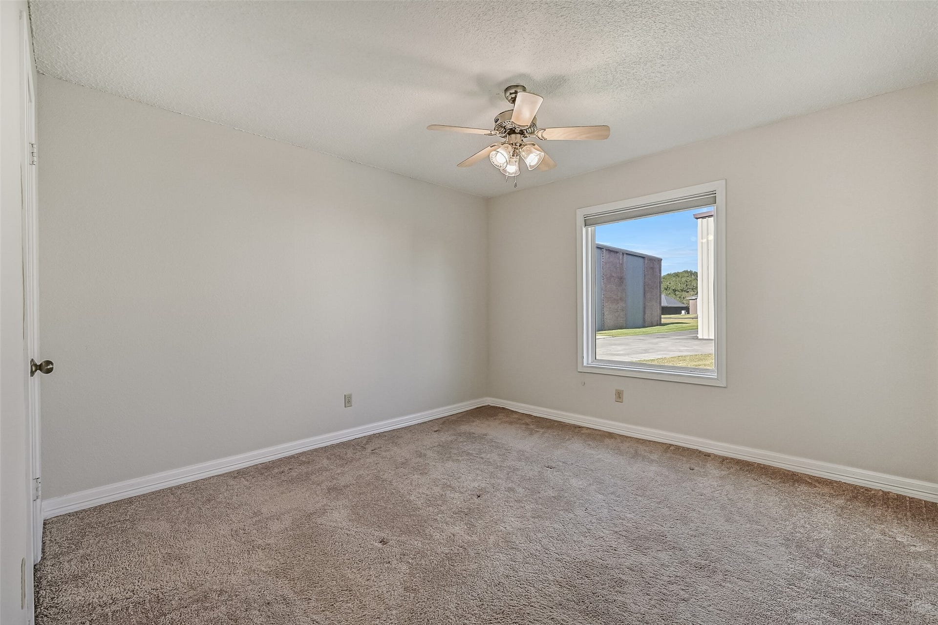Located on the first floor, the third bedroom features neutral carpeting, soft wall colors & a ceiling fan with lighting. A large window overlooks the driveway and neighboring hangars, bringing natural light into the room. This versatile space could also serve as a home office or hobby room.