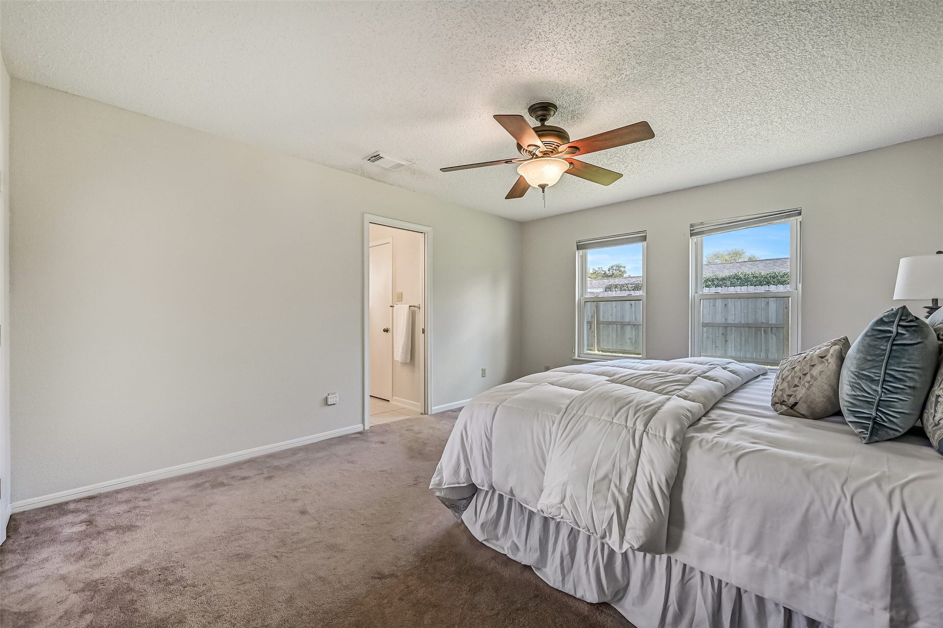 Two windows bring natural light into the primary bedroom, which offers plenty of space for a king-size bed and additional furnishings. Neutral finishes create a versatile backdrop, while the adjoining bathroom and generous closet space add convenience to this first-floor suite.