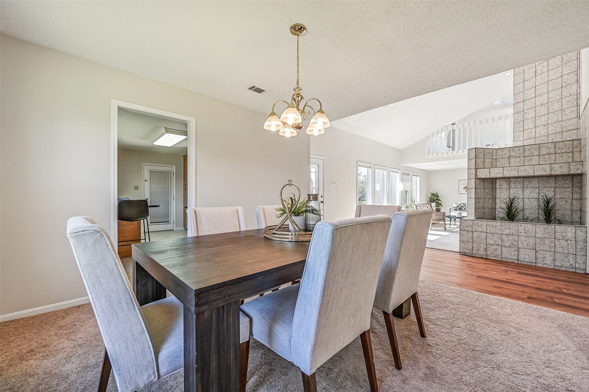 The dining room enjoys an open connection to the living area, allowing natural light to carry throughout the main living spaces. A traditional chandelier adds warmth overhead, while the nearby kitchen provides convenient access for serving meals & hosting gatherings.