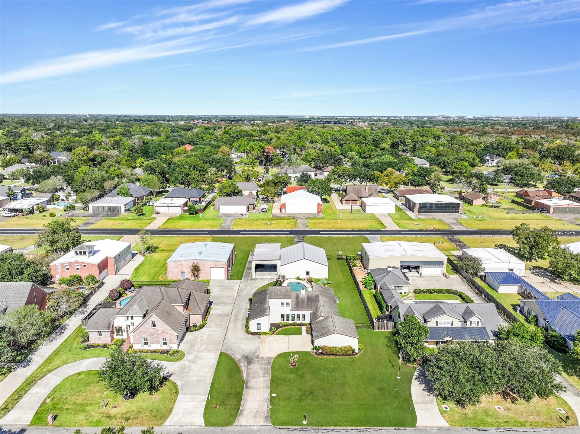 An elevated view showcases the unique layout of this Polly Ranch Estates property! The home, backyard pool, private airplane hangar & adjoining RV garage are all visible, with a separate driveway extending alongside the house. The community's asphalt runway runs directly behind the property.