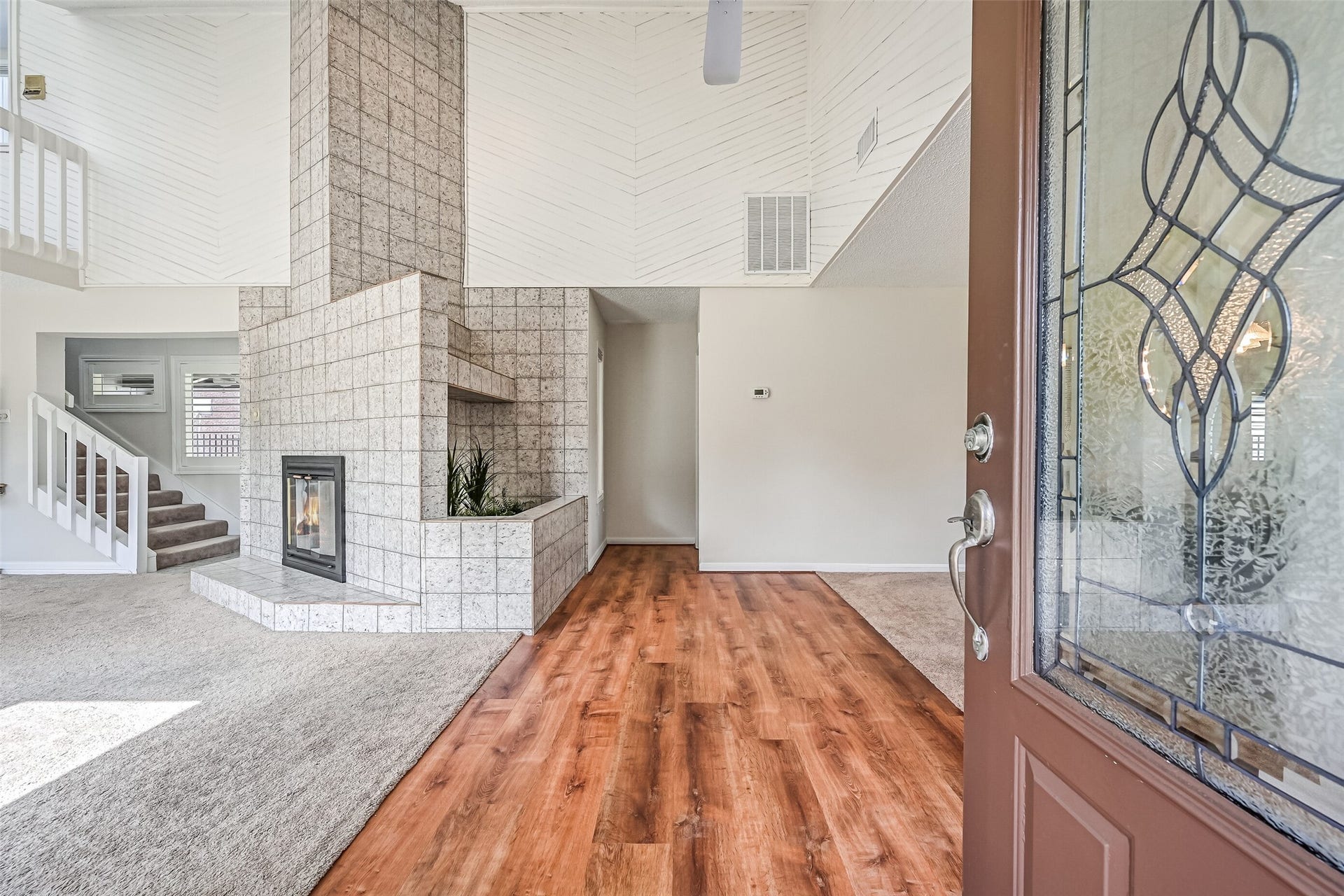 Step inside through the decorative leaded-glass front door to discover an impressive two-story living space! Warm wood-look flooring welcomes you into the entry, where a dramatic tiled wood-burning fireplace, soaring ceiling & staircase to the upstairs loft immediately capture your attention.