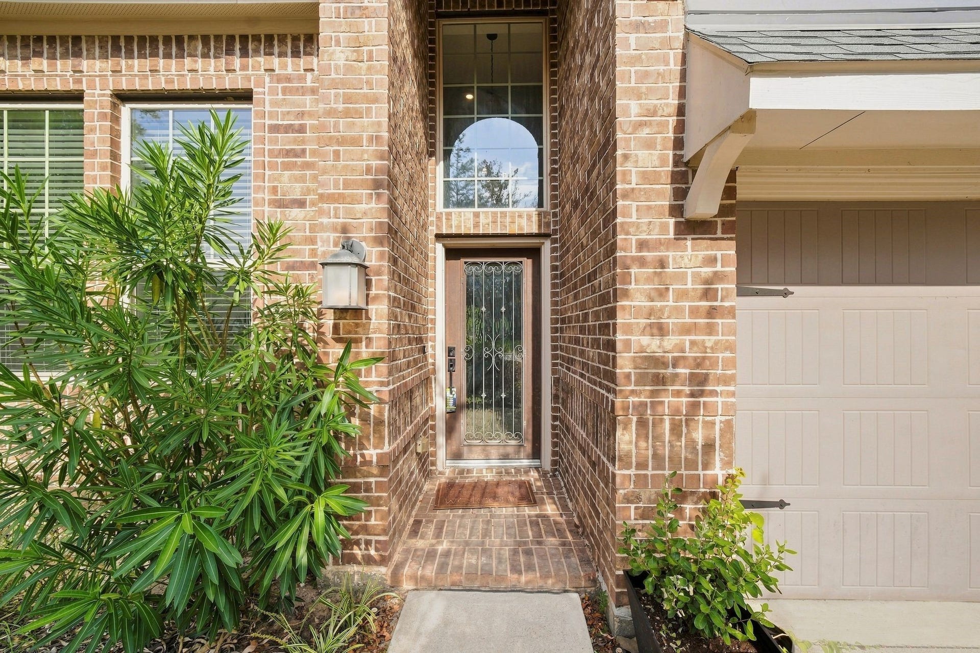 Charming brick exterior with a welcoming front entry, accented by lush greenery and a stylish wrought iron door.