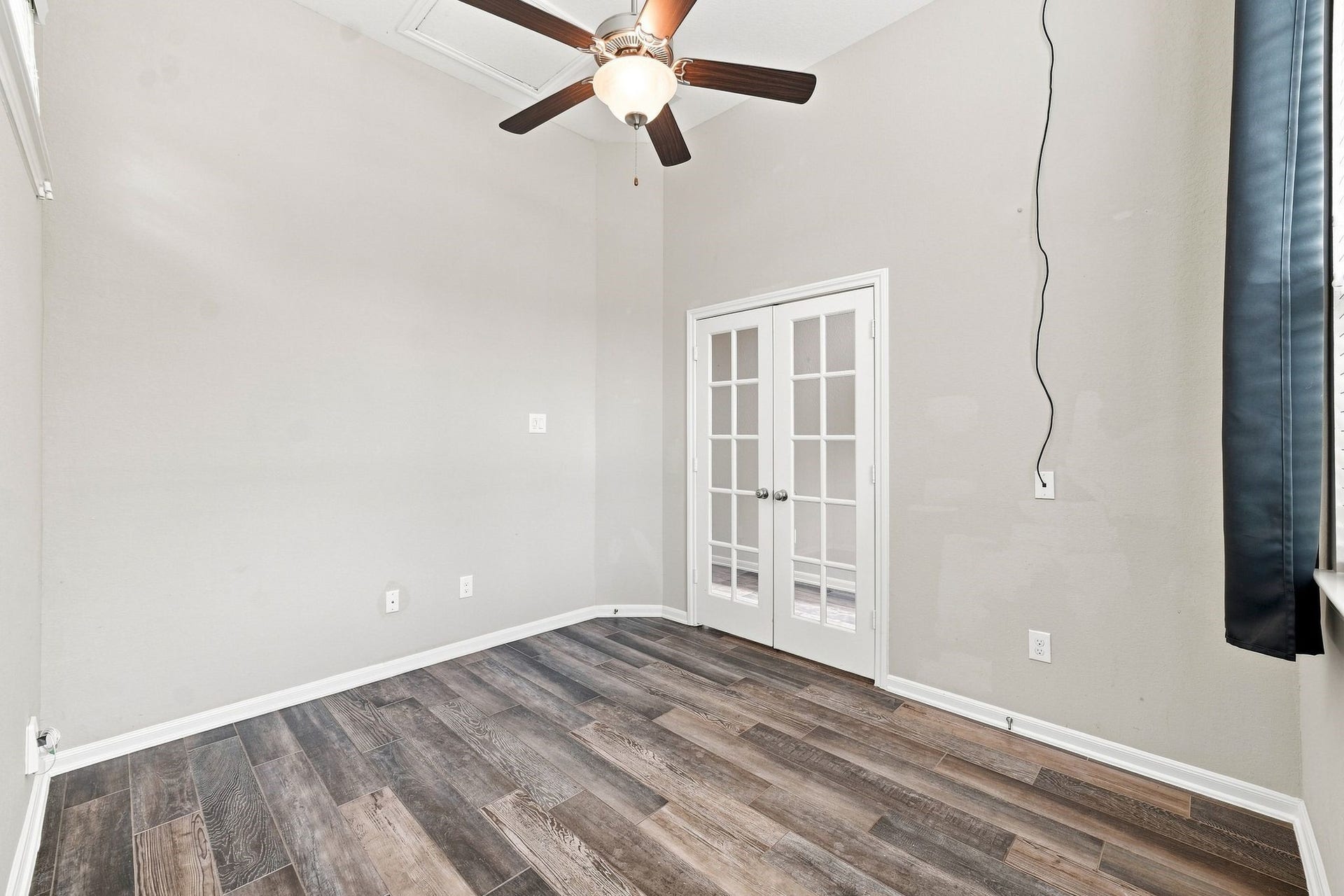 Bright room with elegant wood flooring, a modern ceiling fan, and charming French doors.