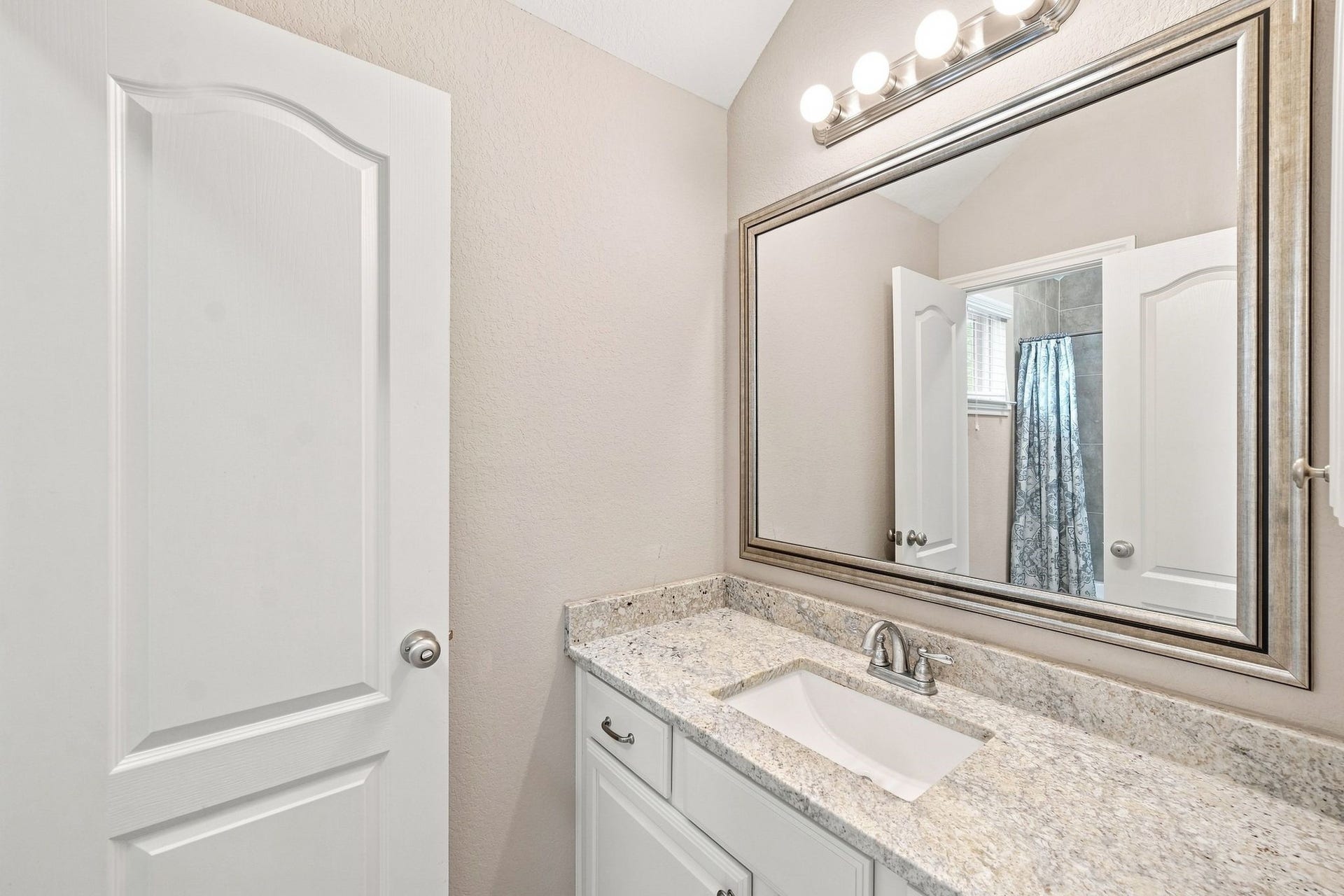 Elegant bathroom featuring a spacious granite countertop, under-mount sink, and a large framed mirror with bright vanity lighting.