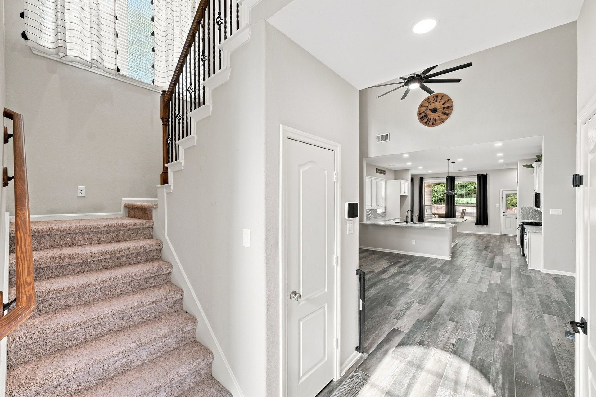 Inviting entryway featuring a stylish staircase, leading to a spacious, open-concept living area with modern flooring and a sleek kitchen, perfect for entertaining.