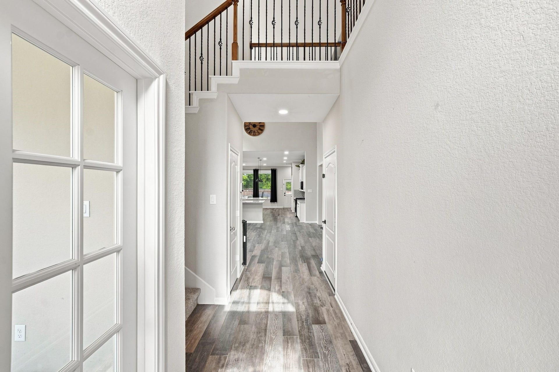 Elegant entryway with high ceilings and wood-look flooring leading to a modern kitchen, accented by stylish railings and abundant natural light.