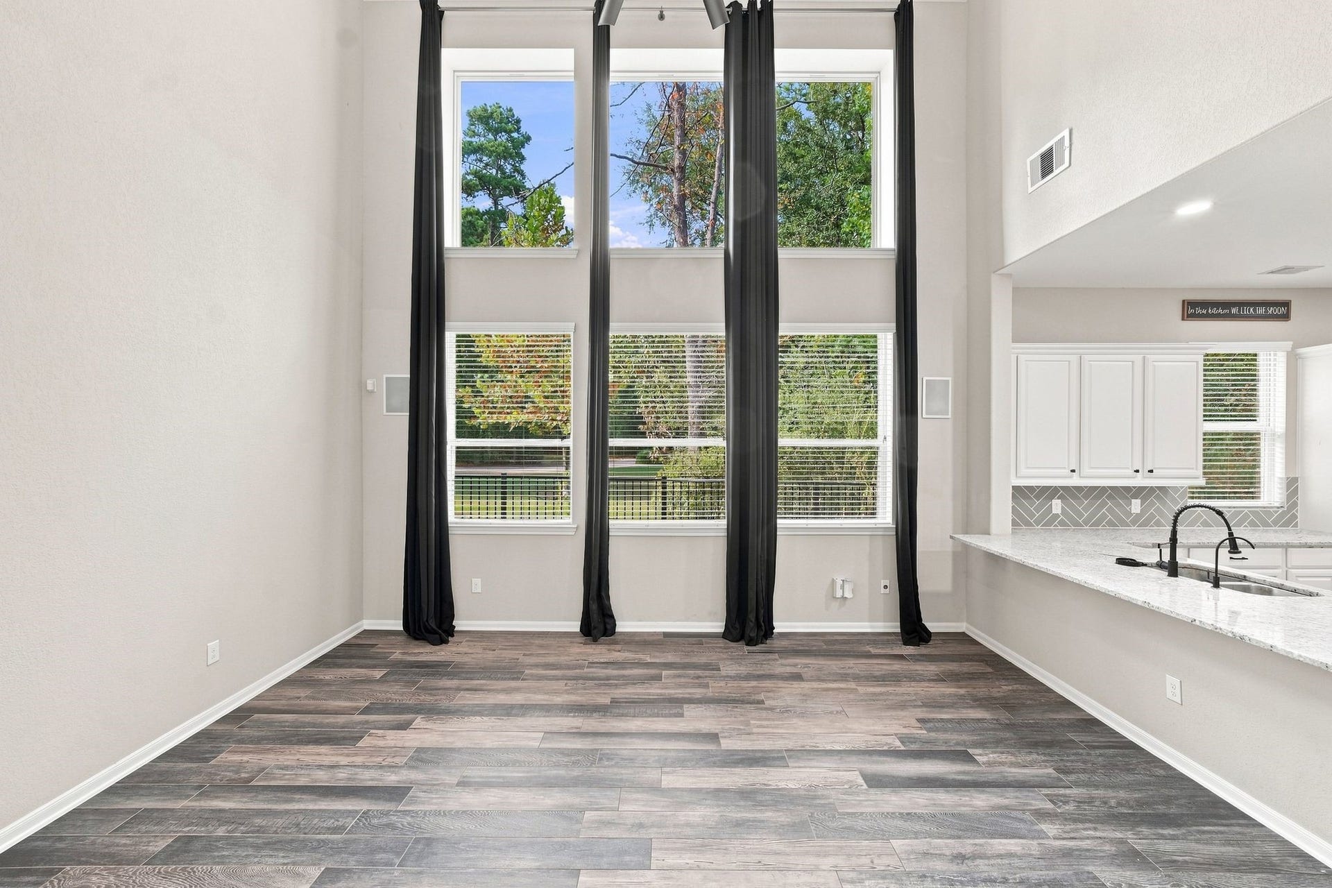 Spacious living area with soaring ceilings and large windows, offering abundant natural light and scenic views. The open layout seamlessly connects to the modern kitchen with sleek countertops.