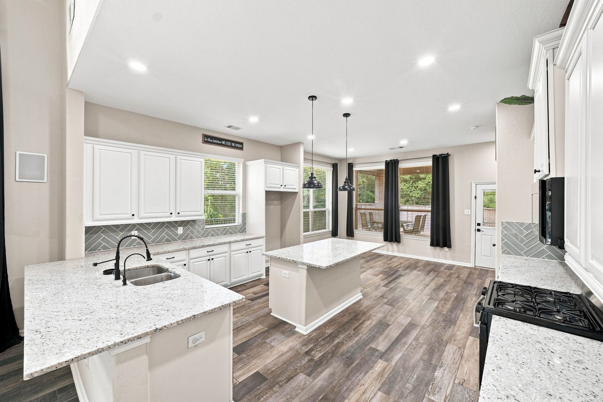 Spacious kitchen with sleek white cabinetry, granite countertops, and a central island. Modern pendant lighting and large windows offer abundant natural light and views of the lush surroundings.