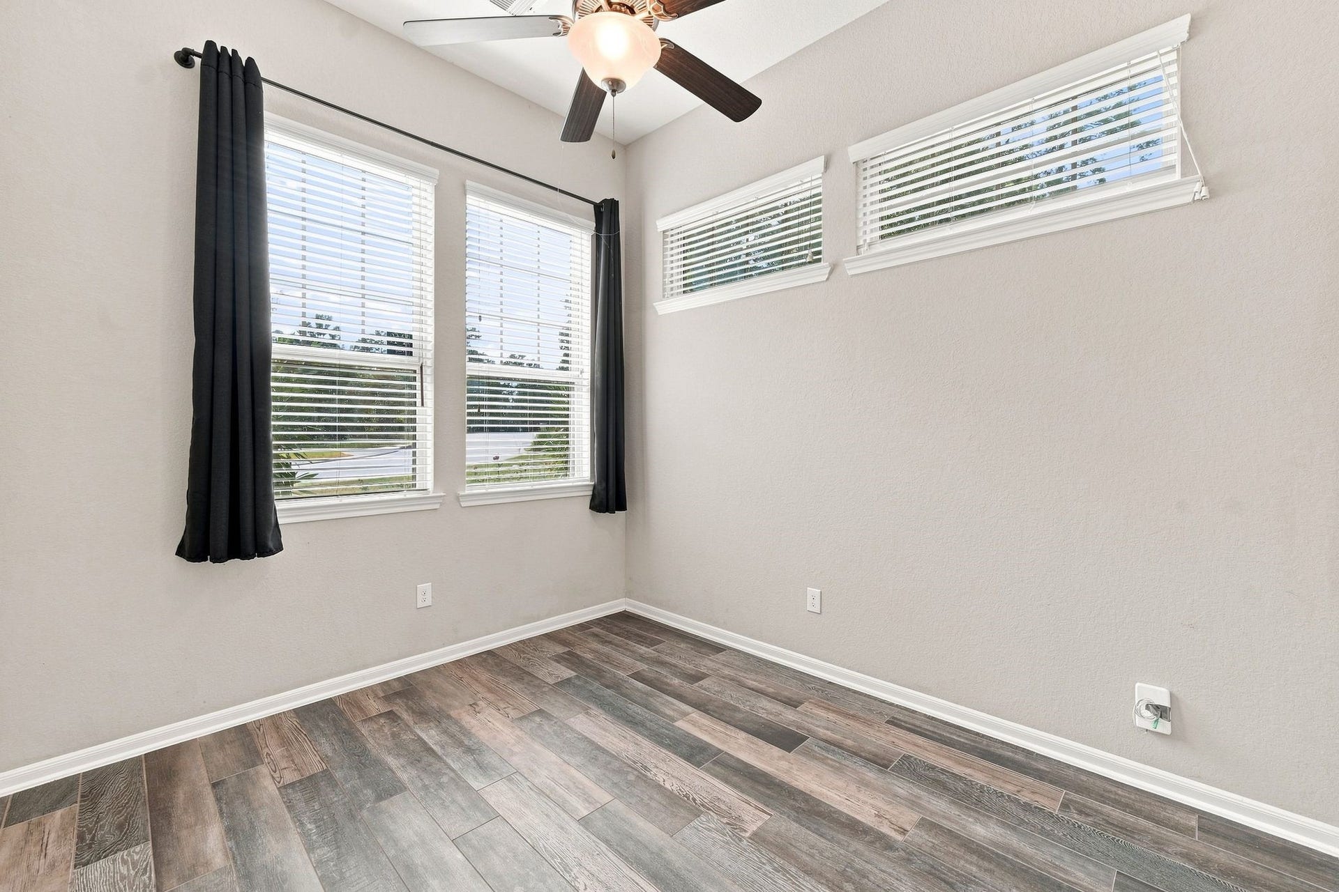 Bright room with large windows, sleek wood-look flooring, and a modern ceiling fan, perfect for a cozy home office or guest room.