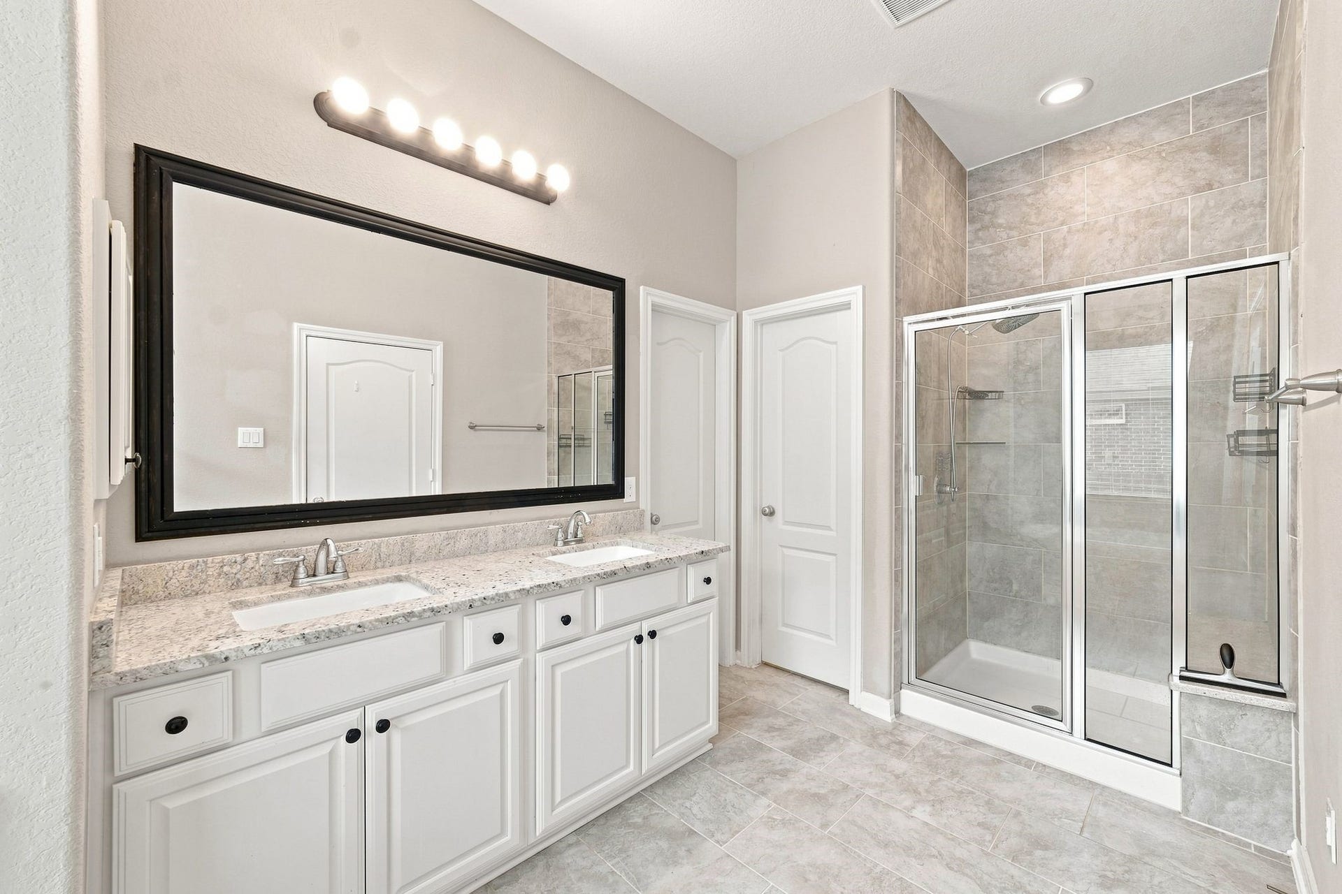 Elegant bathroom featuring a spacious dual-sink vanity with granite countertops, a large mirror, and a modern glass-enclosed shower.