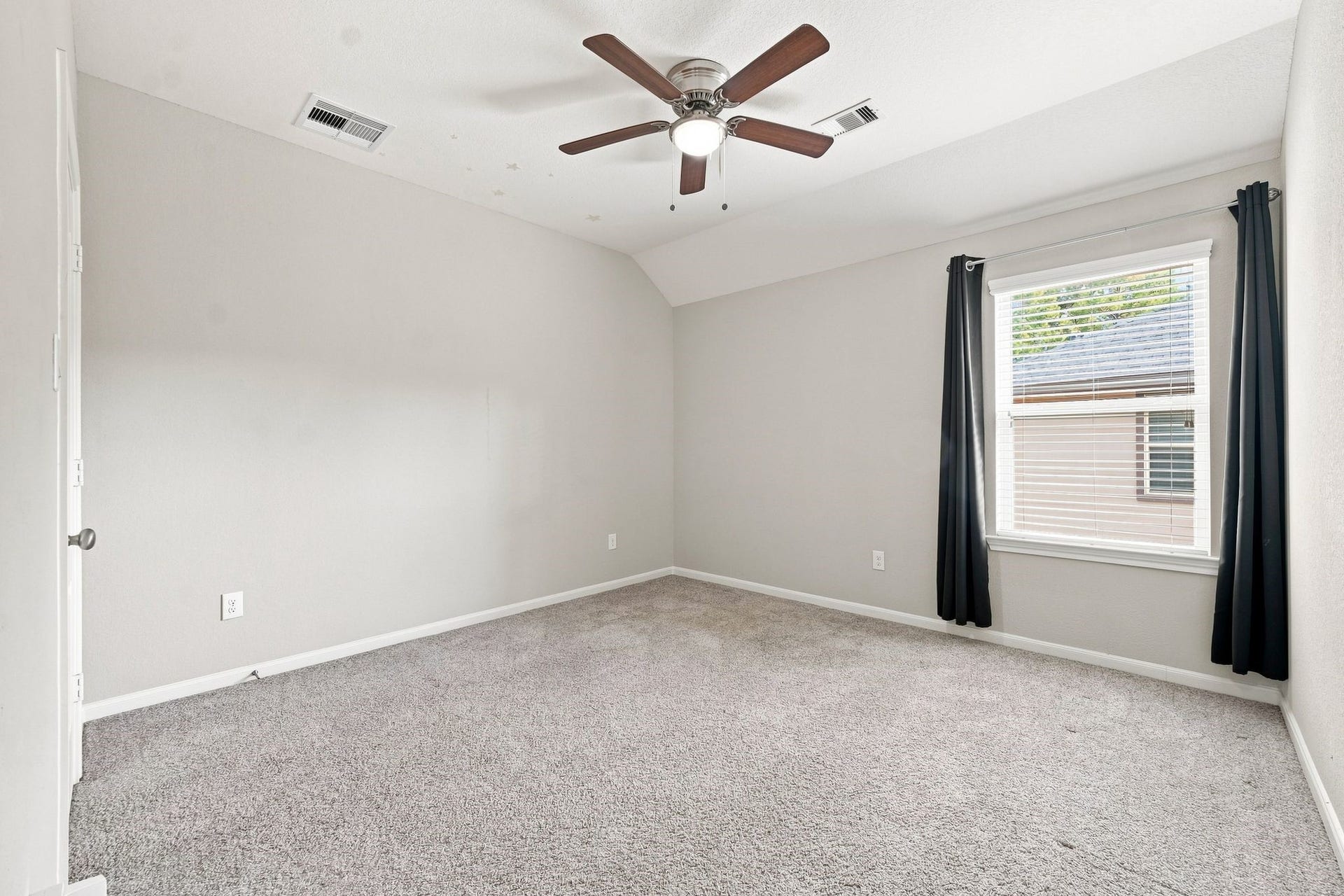 Spacious bedroom with plush carpeting, neutral walls, and a ceiling fan for comfort, complemented by natural light through a well-sized window.