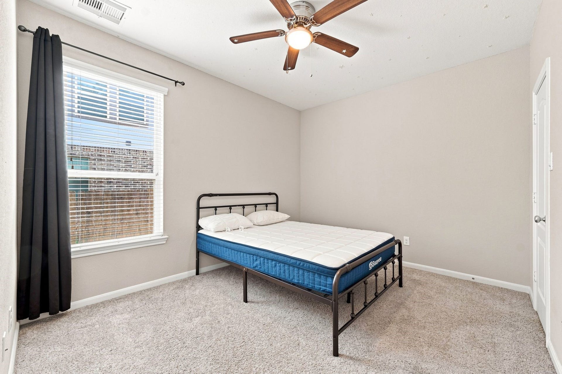 Cozy bedroom with neutral tones features a ceiling fan, ample natural light from a large window, and plush carpeting.