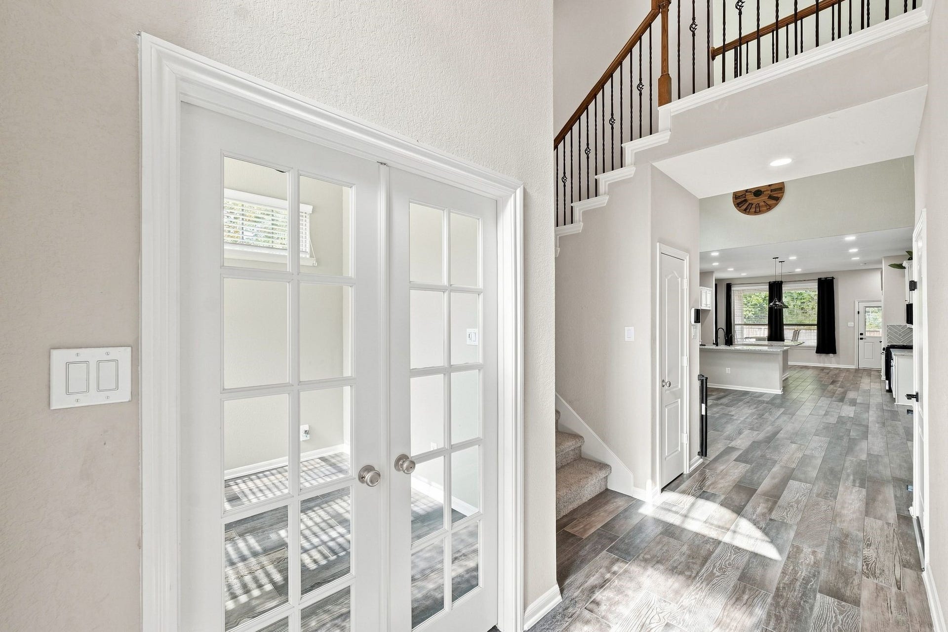 Bright and inviting entryway with elegant French doors, leading to an open-concept living area featuring sleek flooring and a stylish staircase.