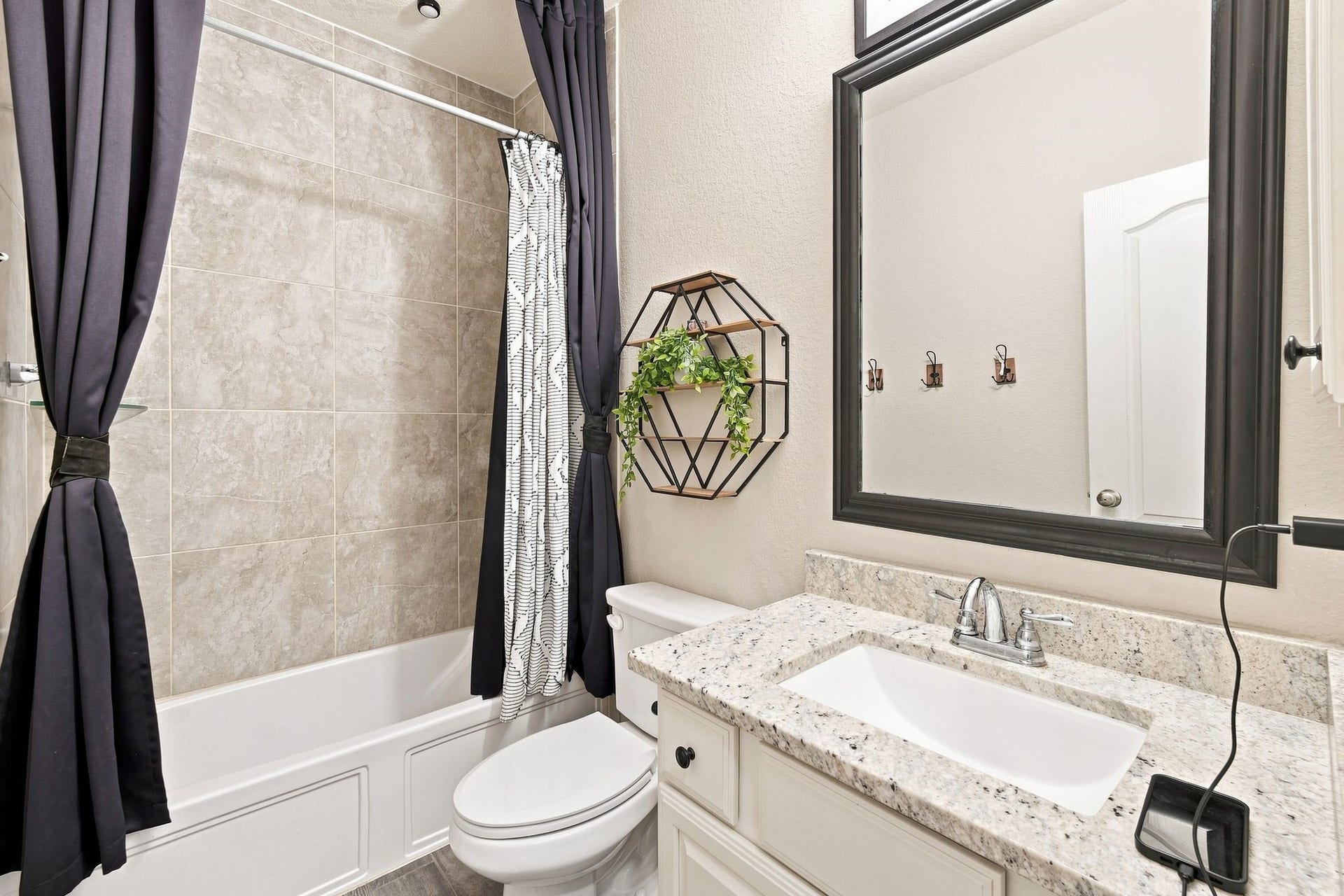 Elegant bathroom featuring a sleek granite countertop, modern fixtures, and stylish tile work. The space is accented by a contemporary mirror and decorative shelving.