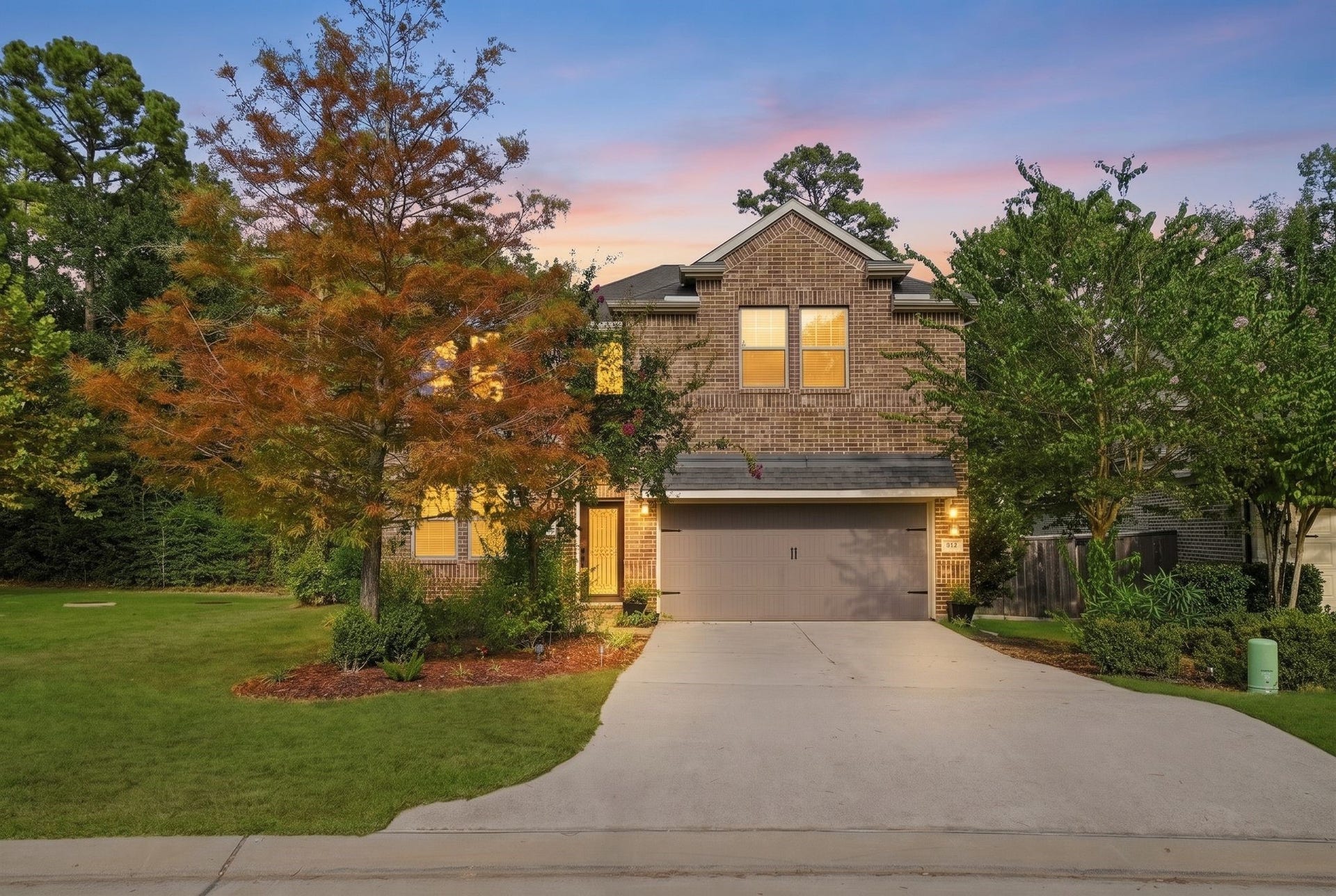 Charming two-story brick home with a spacious driveway and lush landscaping, set against a serene twilight sky.
