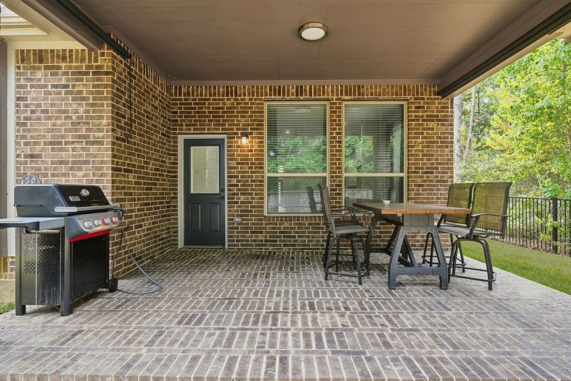 Charming covered patio with brick flooring, perfect for outdoor dining and entertaining, featuring a built-in grill and ample seating space.