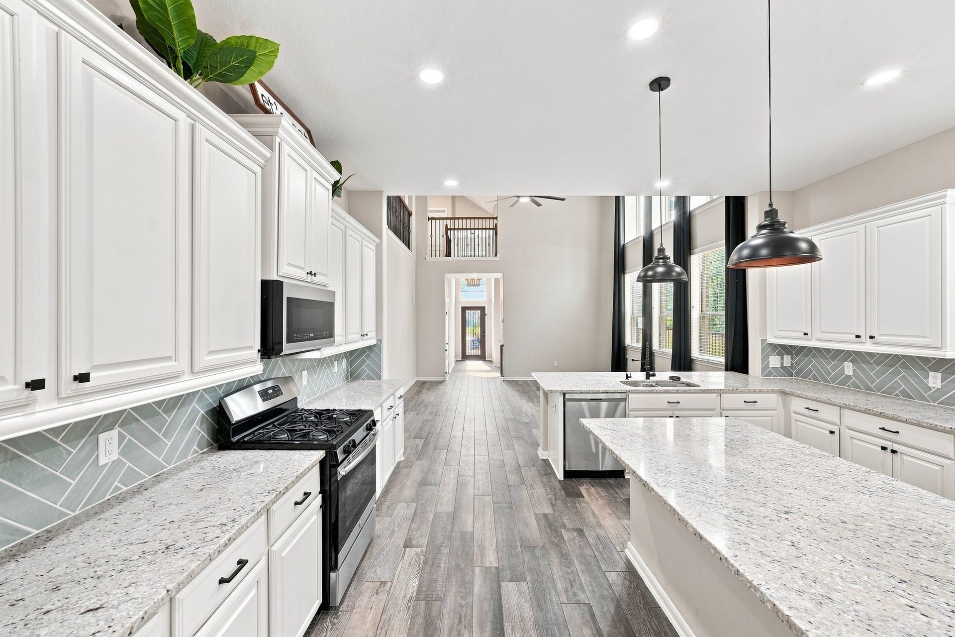 Spacious kitchen with elegant white cabinetry, granite countertops, and a modern backsplash. High ceilings and large windows flood the area with natural light, while sleek pendant lights add a stylish touch.