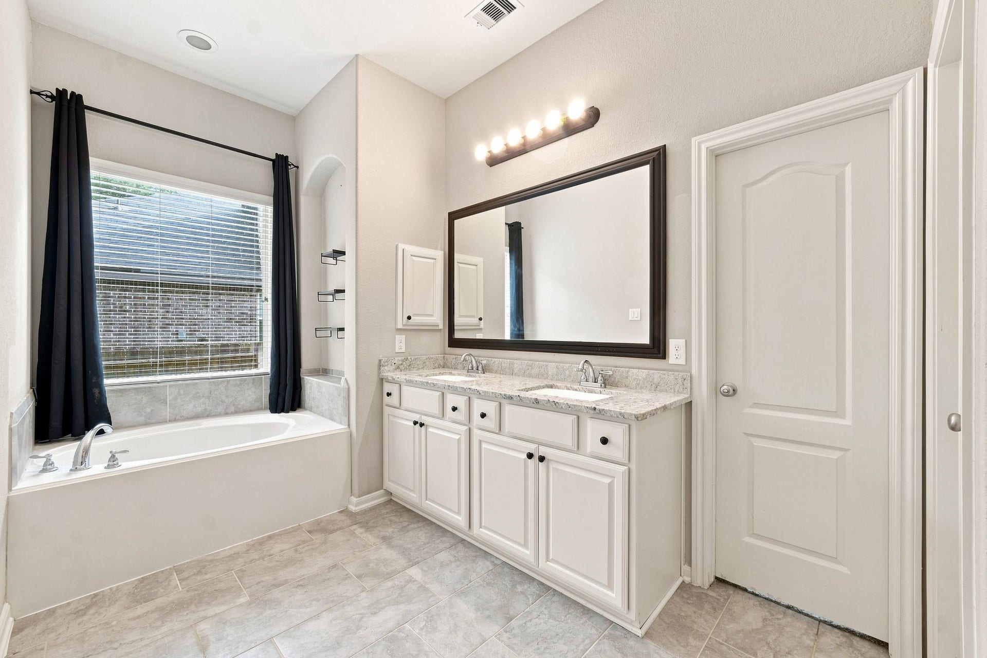 Elegant bathroom featuring a luxurious soaking tub, dual sinks with a marble countertop, and ample storage space, all bathed in natural light.