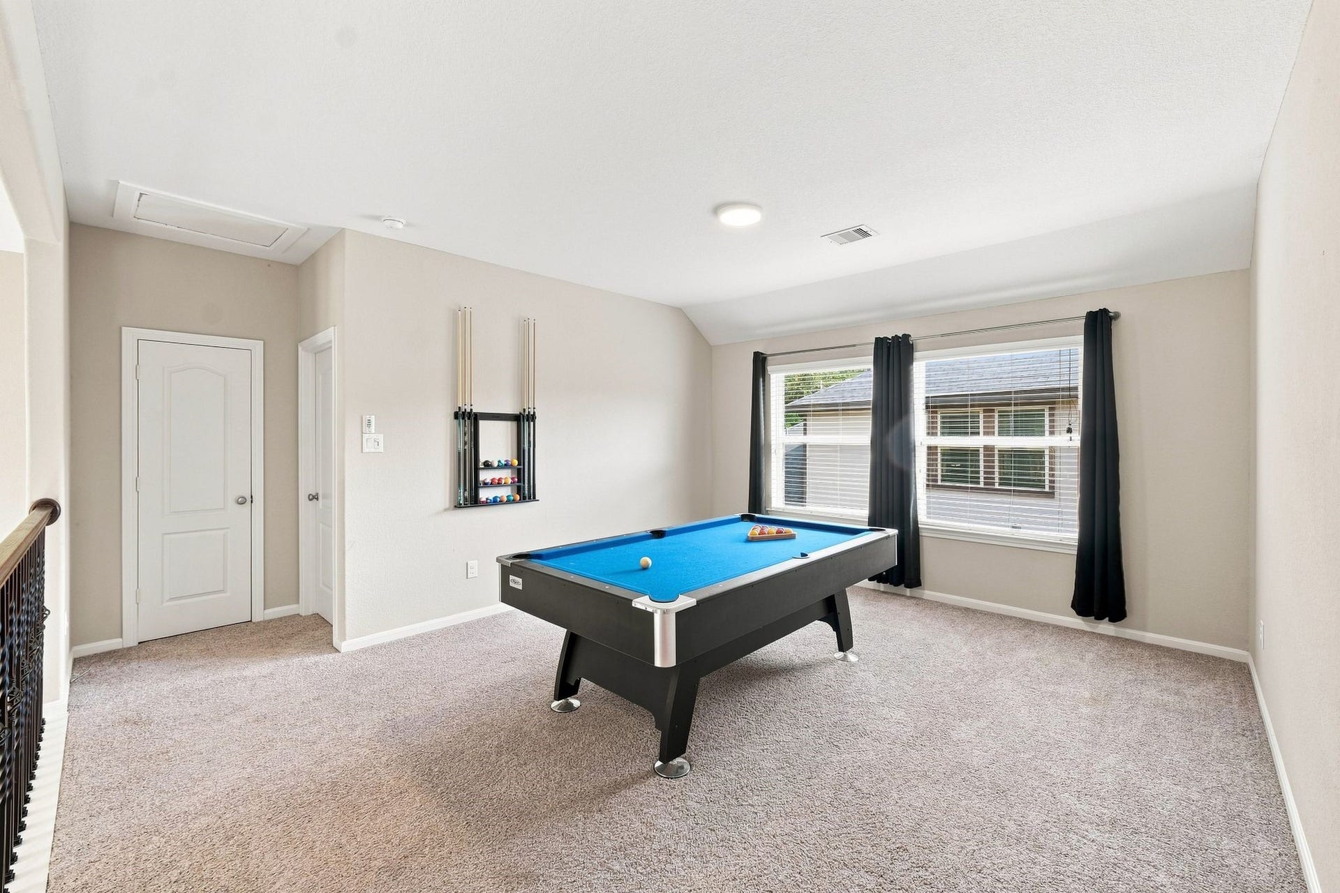Spacious game room featuring a stylish pool table, plush carpeting, and abundant natural light from a large window with elegant drapes.
