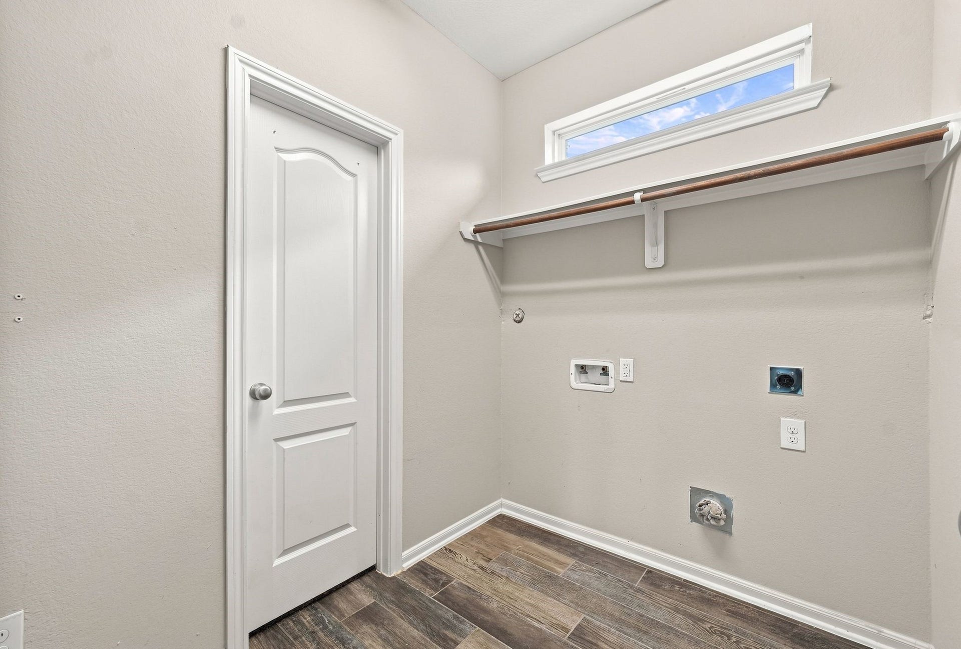 Spacious laundry room featuring modern hookups, a convenient shelf for storage, and elegant wood-look tile flooring.