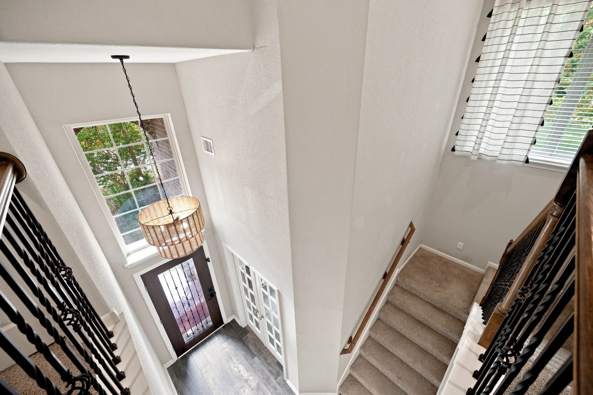 Elegant entryway featuring a tall ceiling, stylish chandelier, and a staircase with wrought iron railings, offering a warm welcome and abundant natural light.