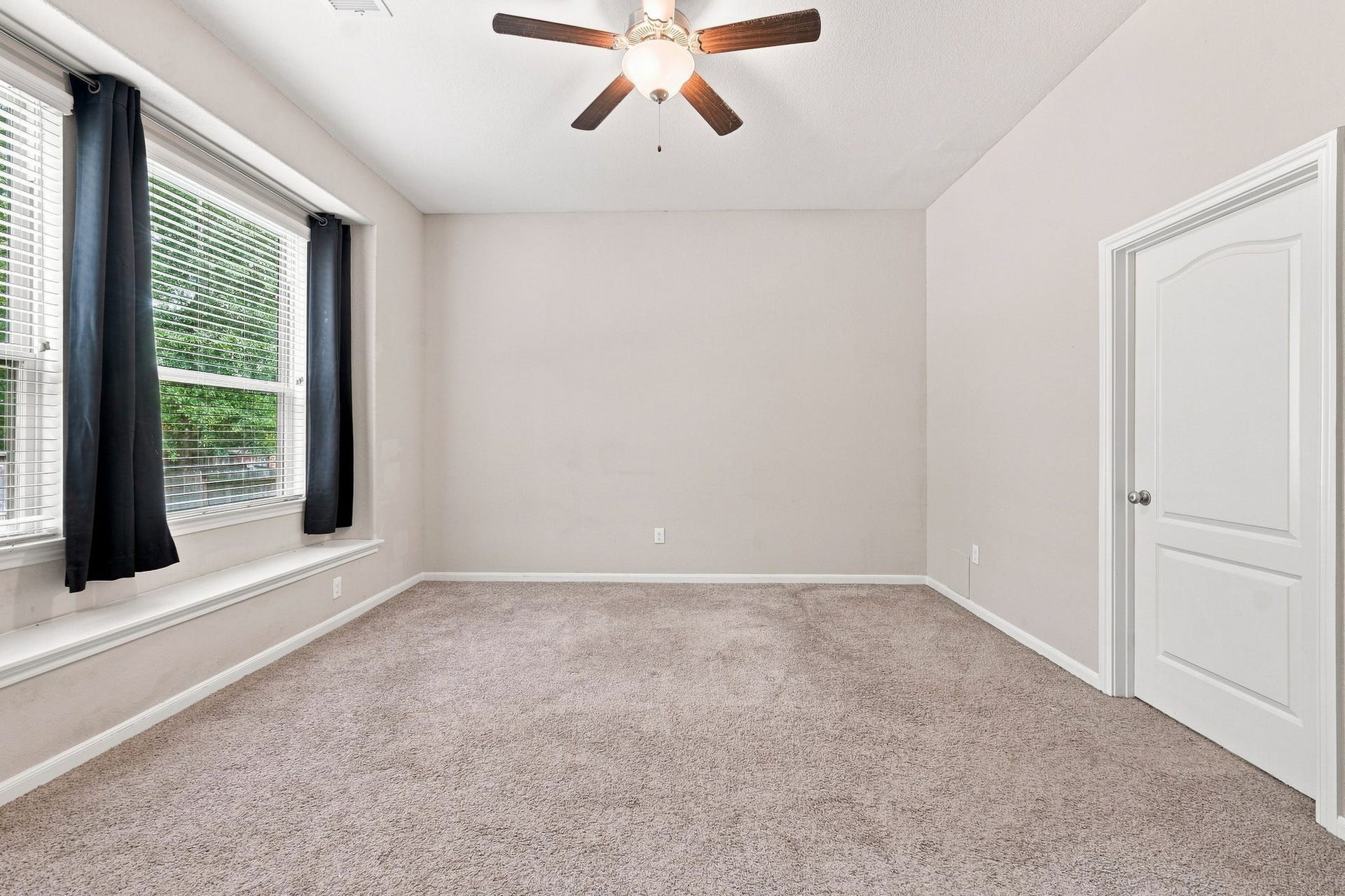 Spacious room with plush carpeting, large windows for natural light, and a ceiling fan for comfort.