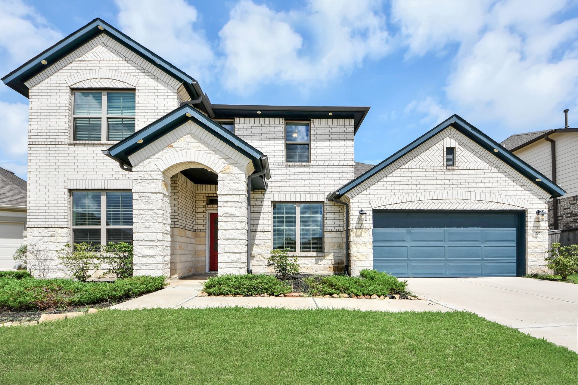 4707 Great Acre Lane, Fresno, TX 77545 Stunning two-story home featuring elegant white brick exterior, modern blue accents, and a spacious two-car garage, set on a well-manicured lawn.