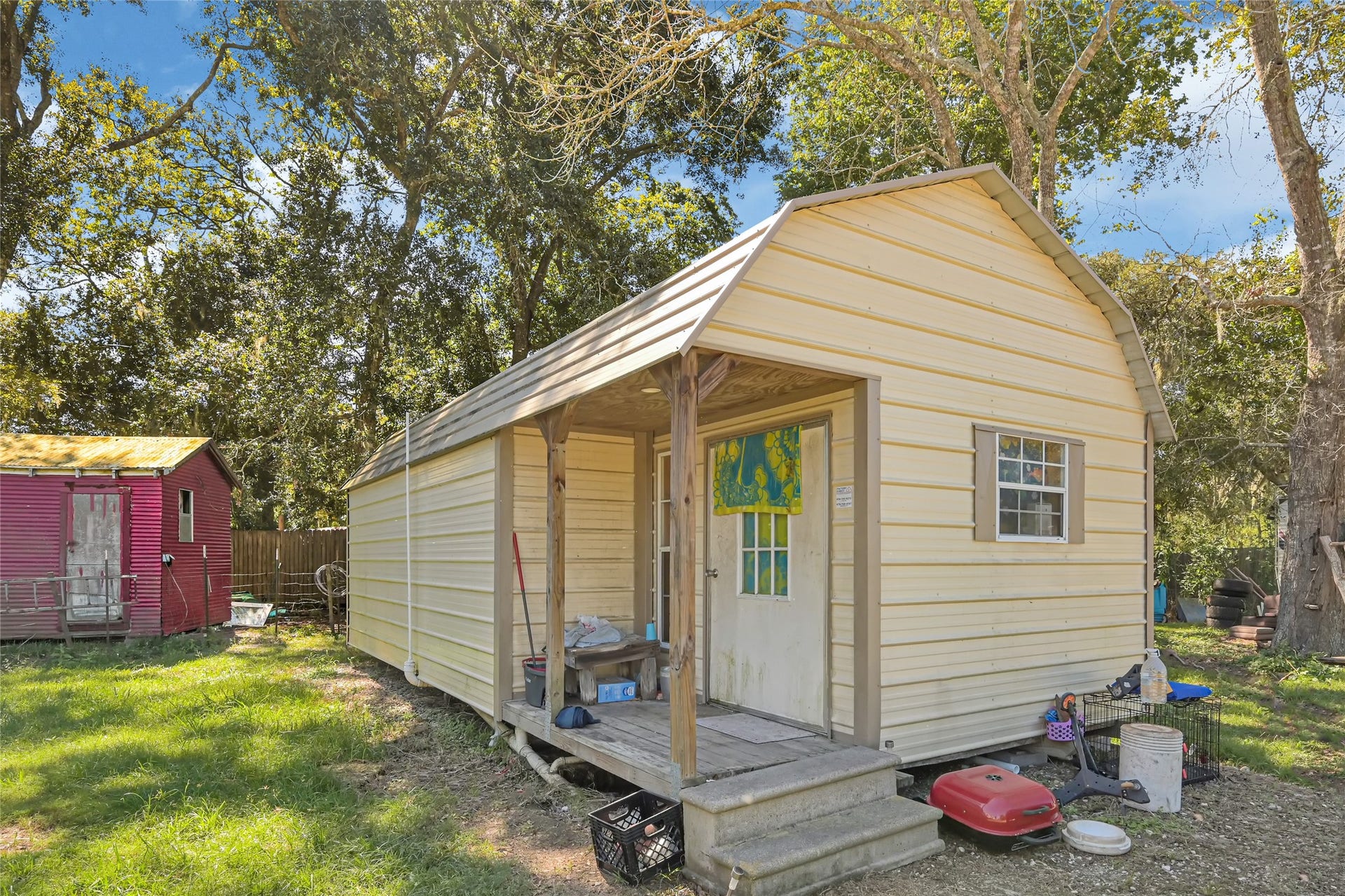 121 Patterson Road, #CR814, Brazoria, TX 77422 Charming backyard retreat featuring a cozy shed with a welcoming porch, nestled amidst lush greenery, perfect for storage or a personal getaway.