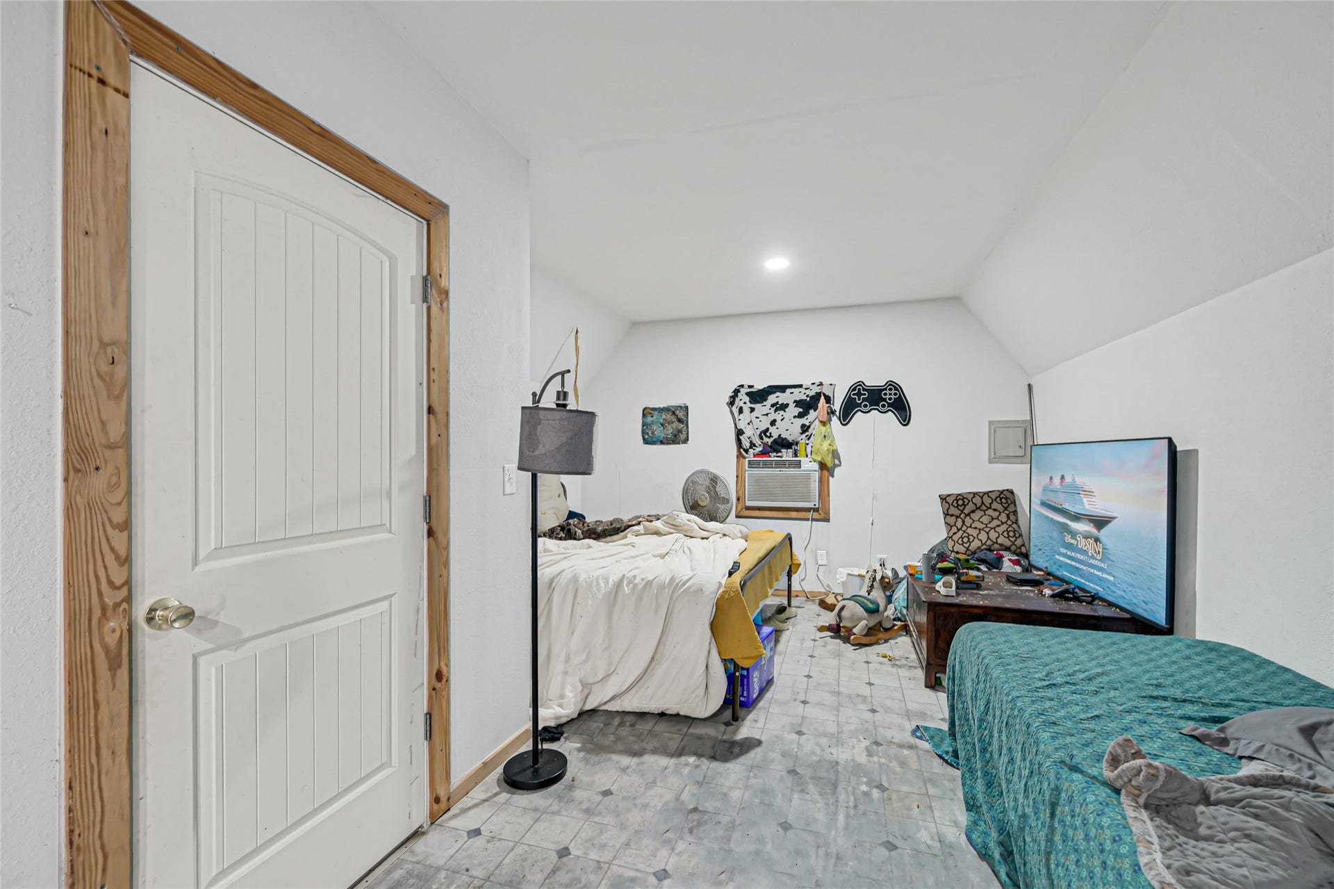121 Patterson Road, #CR814, Brazoria, TX 77422 Cozy bedroom with sloped ceilings, featuring a bed, a TV, and a window air conditioner for climate control.