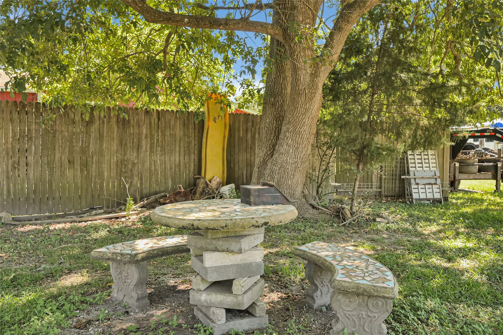 121 Patterson Road, #CR814, Brazoria, TX 77422 Charming backyard retreat with a mosaic stone table and benches under the shade of mature trees, perfect for relaxing and enjoying nature.