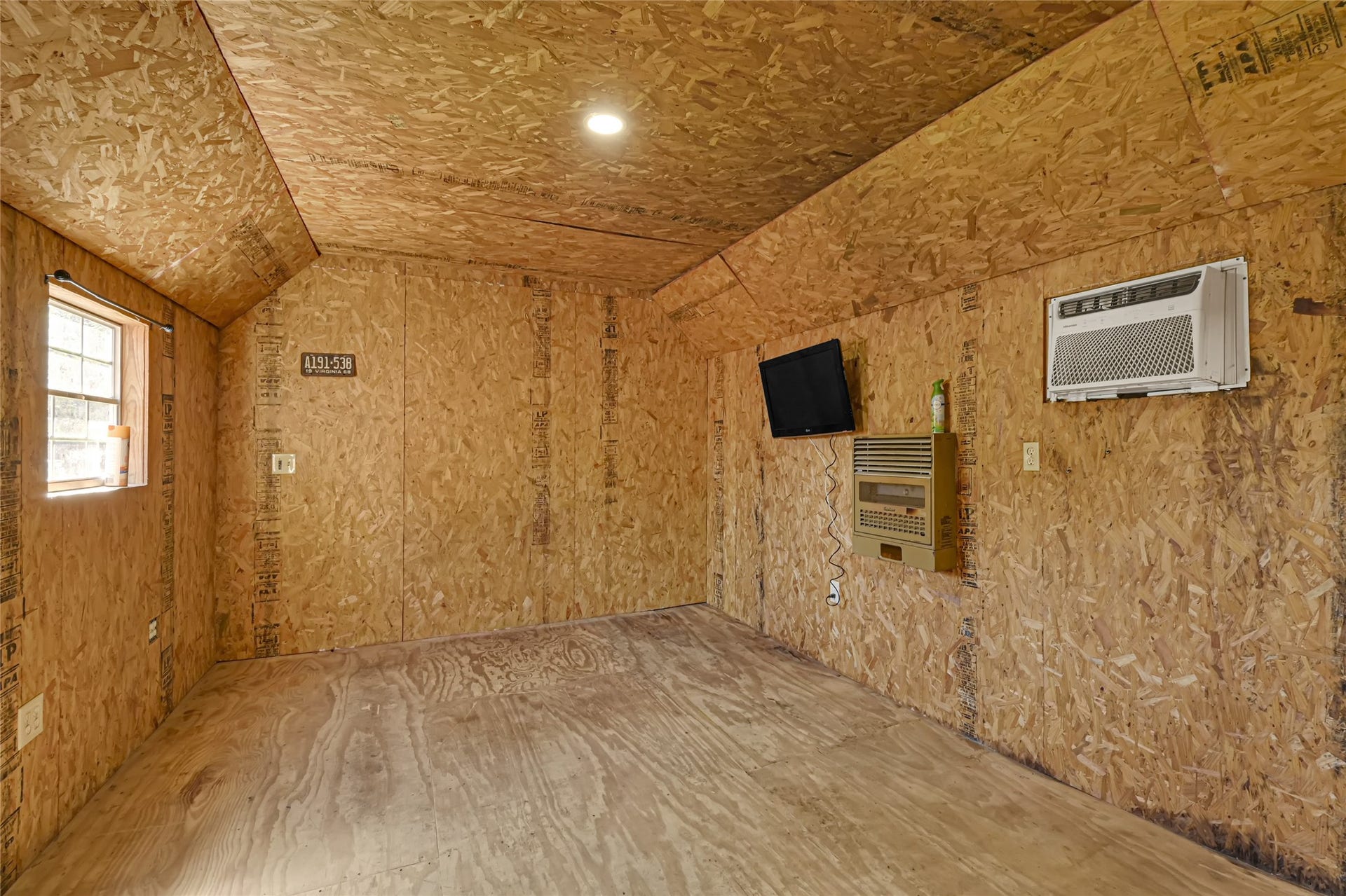 121 Patterson Road, #CR814, Brazoria, TX 77422 Cozy and versatile room with natural wood paneling, featuring a window for ample daylight, wall-mounted air conditioning, and heating unit for year-round comfort.