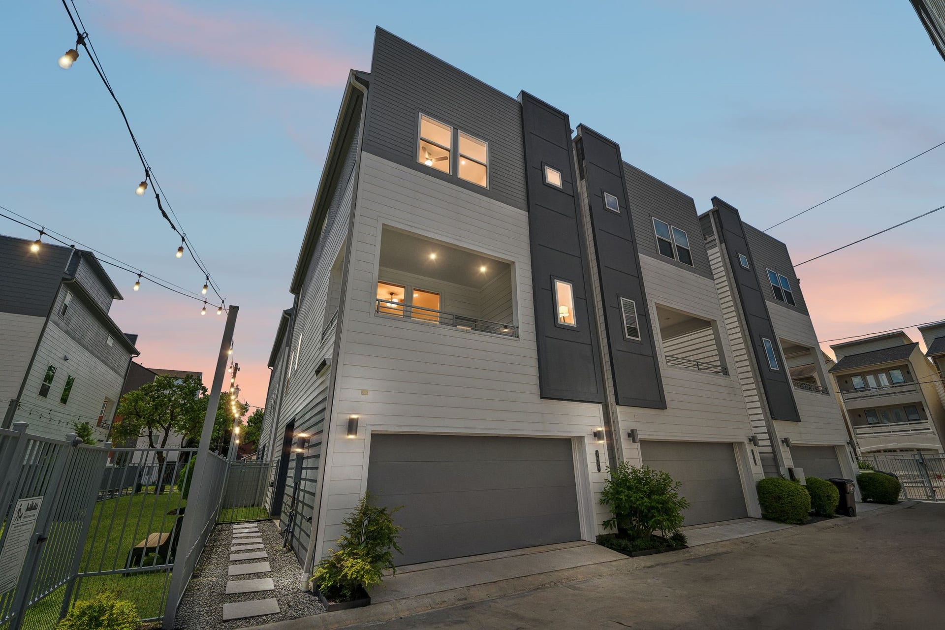 Modern architectural elegance meets urban convenience in this striking multi-level home, featuring sleek lines, ample windows, and a spacious garage, all set against the backdrop of a serene sunset sky.