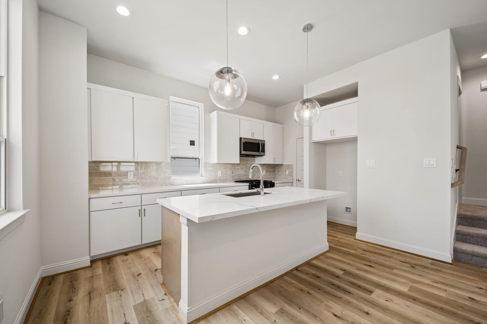 Experience modern elegance in this bright kitchen, featuring sleek white cabinetry, a spacious island with a waterfall countertop, and stylish pendant lighting that complements the warm wood flooring.