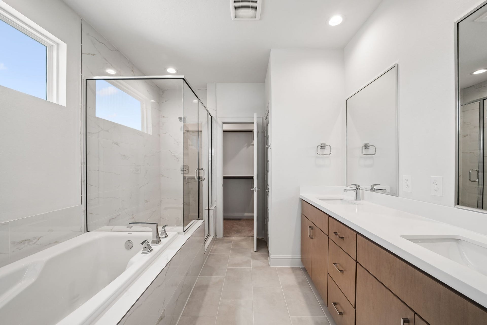 Experience luxury in this elegant primary bathroom, featuring a spacious glass-enclosed shower, a relaxing soaking tub, and a sleek double vanity with ample storage.