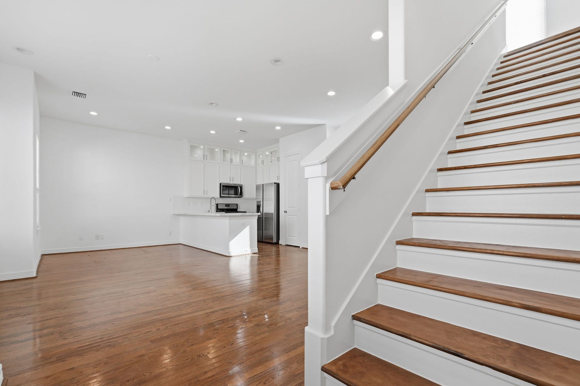 3882 Center Street, Houston, TX 77007 The staircase features rich wood treads, crisp white risers, and a coordinating handrail, creating a striking architectural detail alongside the open-concept living area and kitchen.