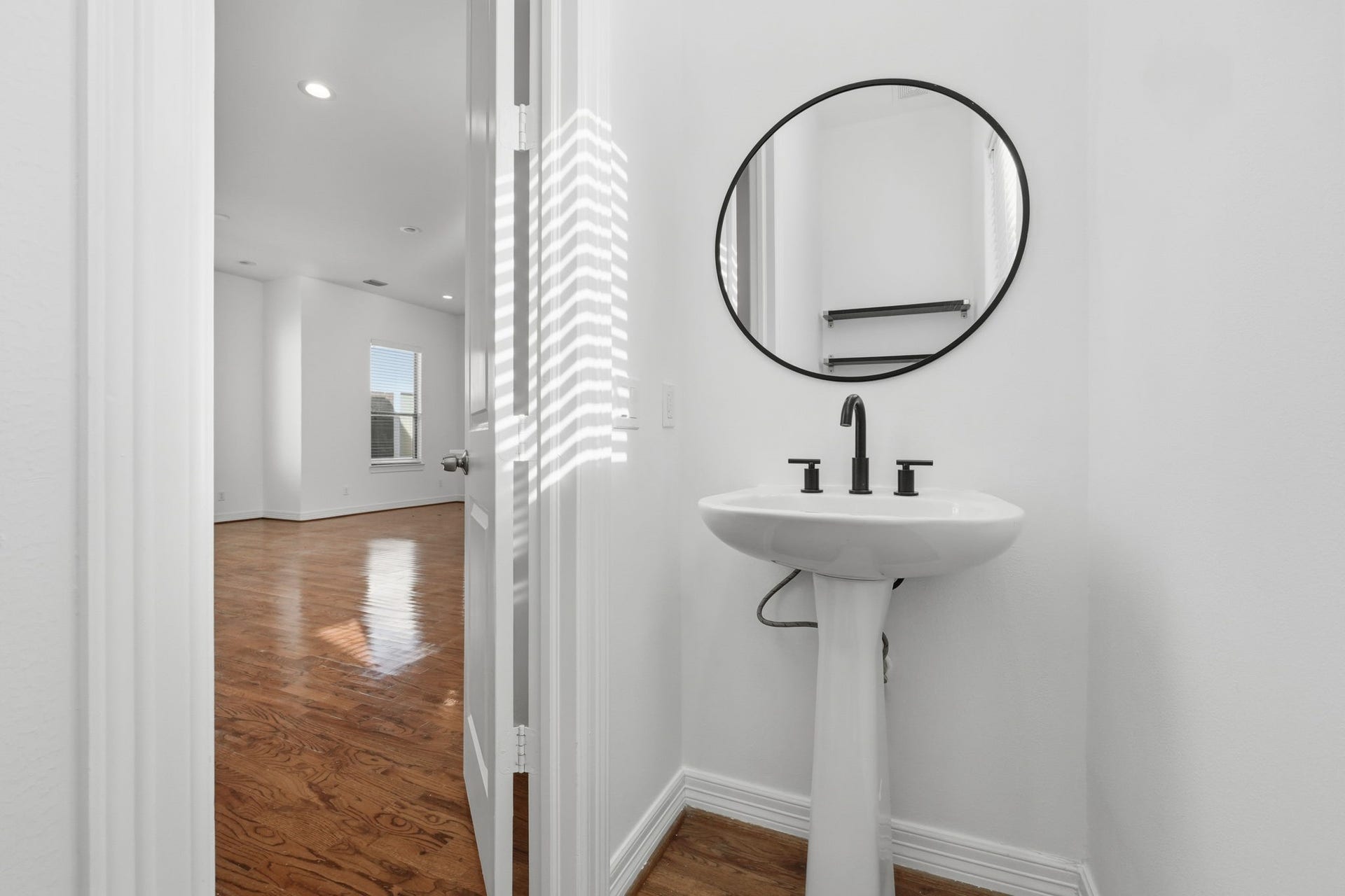 3882 Center Street, Houston, TX 77007 A conveniently placed powder bath features a sleek pedestal sink, round mirror, and modern fixtures, with a clean, neutral design that complements the homes contemporary interior. (2nd floor)