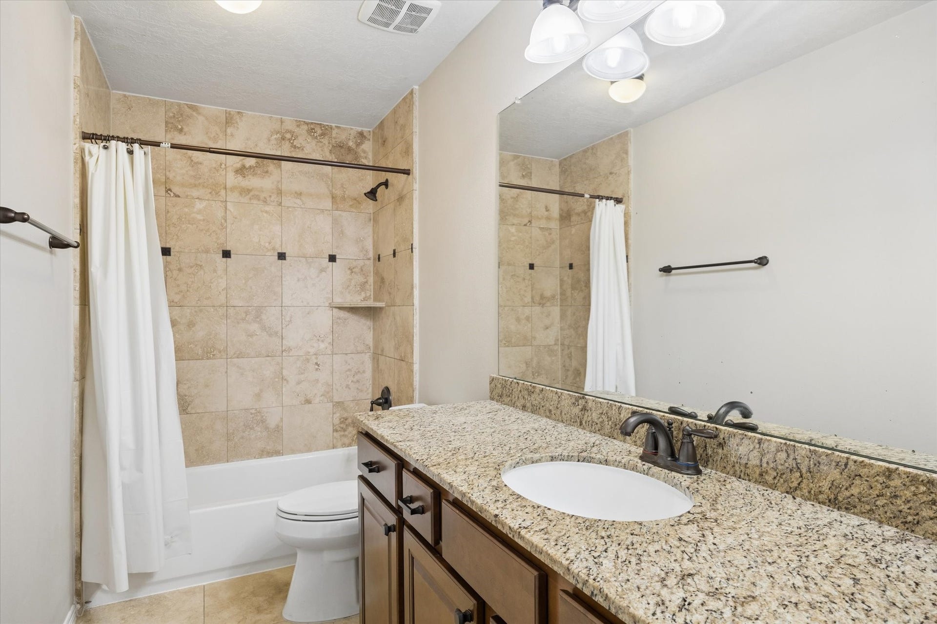 24935 Waterstone Estates Circle W, Tomball, TX 77375 Private en-suite bathroom featuring a granite countertop and a tiled tub and shower combination, offering added comfort and convenience for family members or overnight guests.