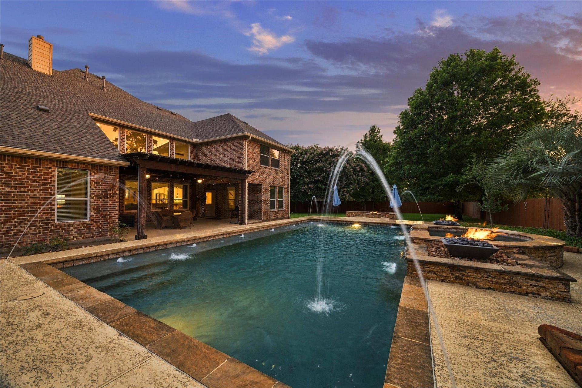 24935 Waterstone Estates Circle W, Tomball, TX 77375 A captivating evening view showcasing the expansive pool, striking water features, and warm fire accents, creating a truly memorable backdrop for outdoor living and entertaining.