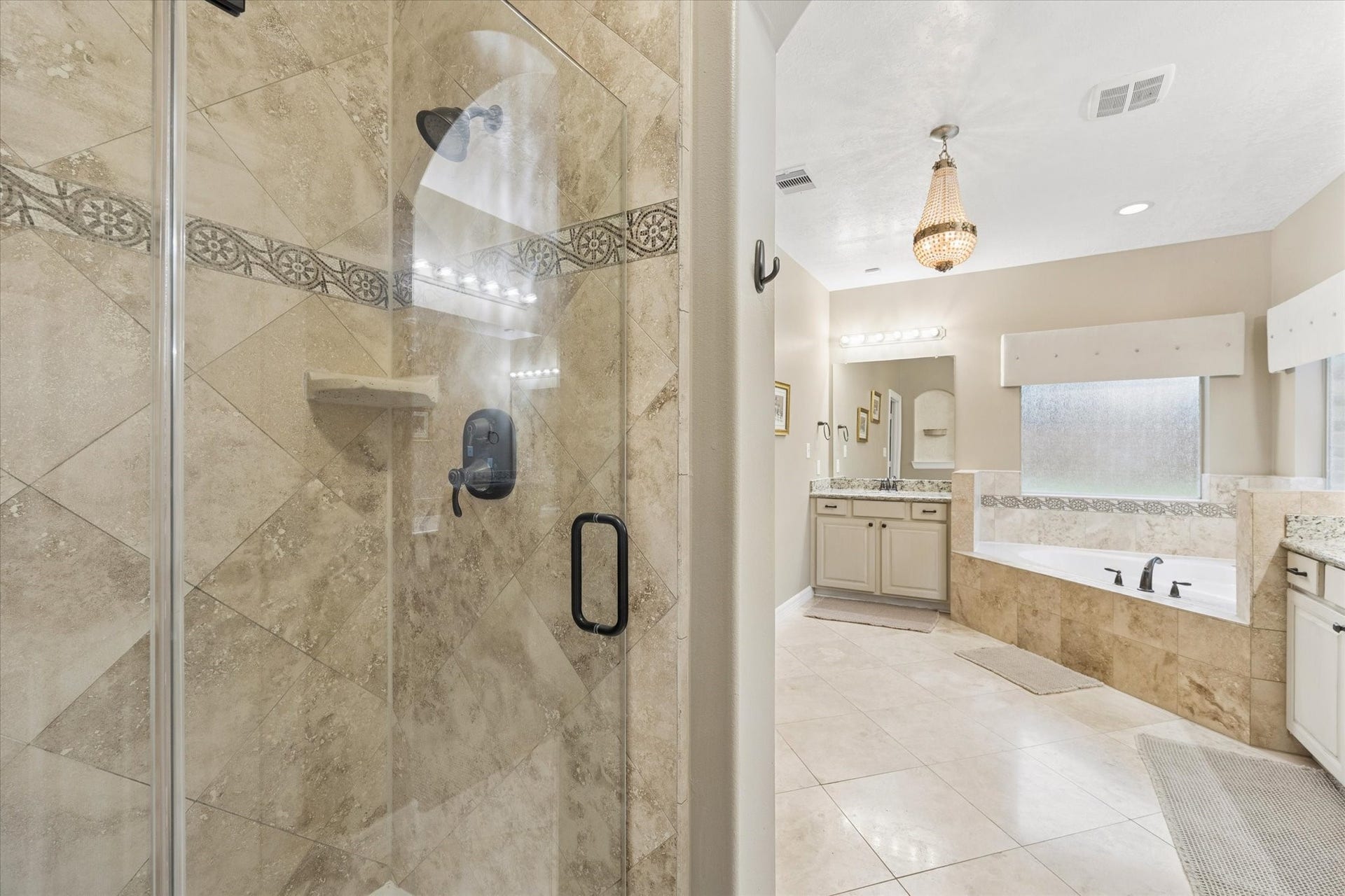24935 Waterstone Estates Circle W, Tomball, TX 77375 A closer view of the generously sized primary en-suite bath highlights the separate walk-in shower with decorative tile accents and glass enclosure, complemented by the jetted soaking tub and dual vanities. Abundant natural light enhances the open, airy atmosphere, creating a relaxing and functional private retreat.