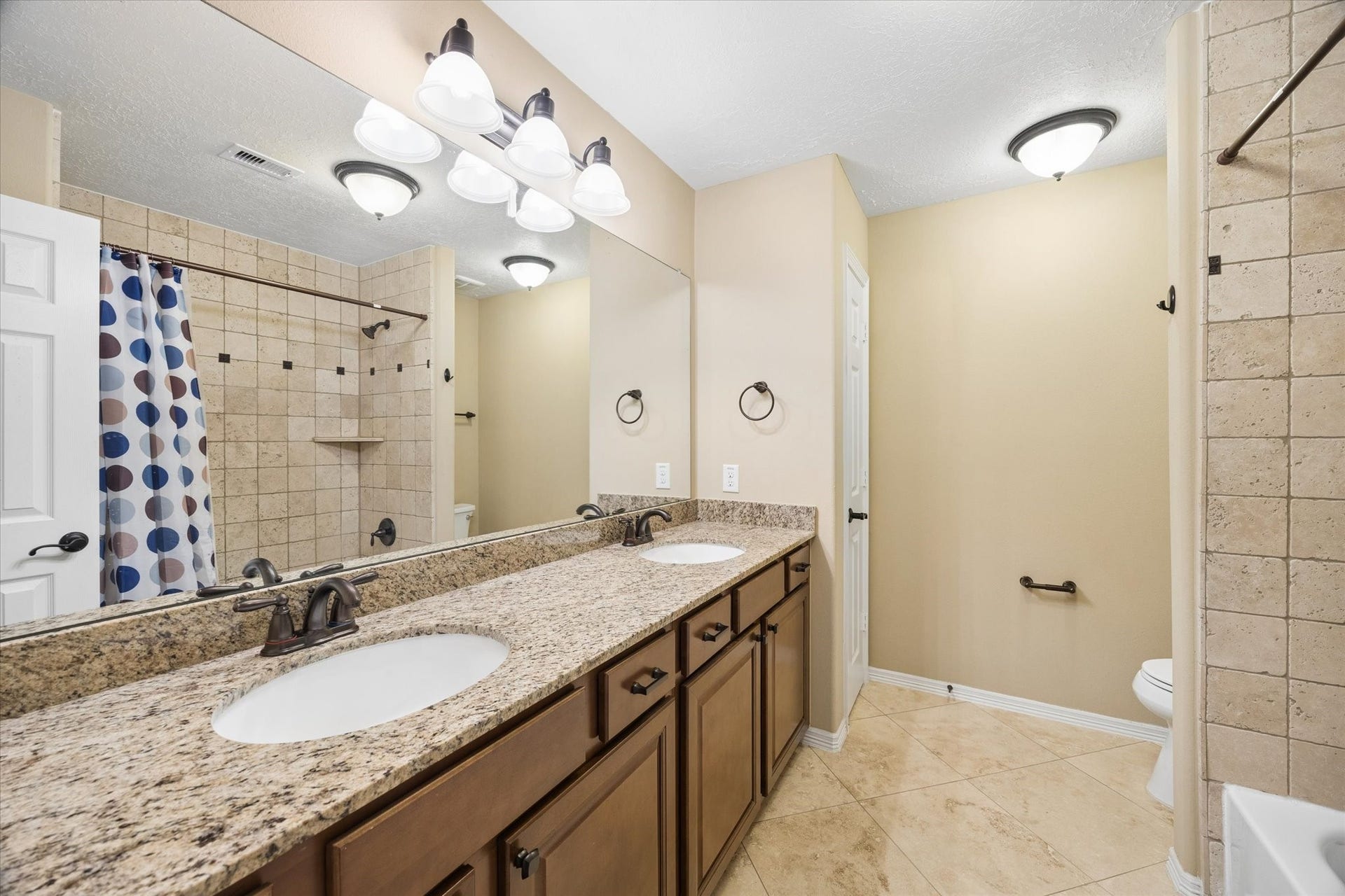 24935 Waterstone Estates Circle W, Tomball, TX 77375 Well-appointed upstairs secondary bathroom featuring an expansive granite countertop, dual sinks, abundant cabinetry, LED lighting, and a tiled tub and shower combination.