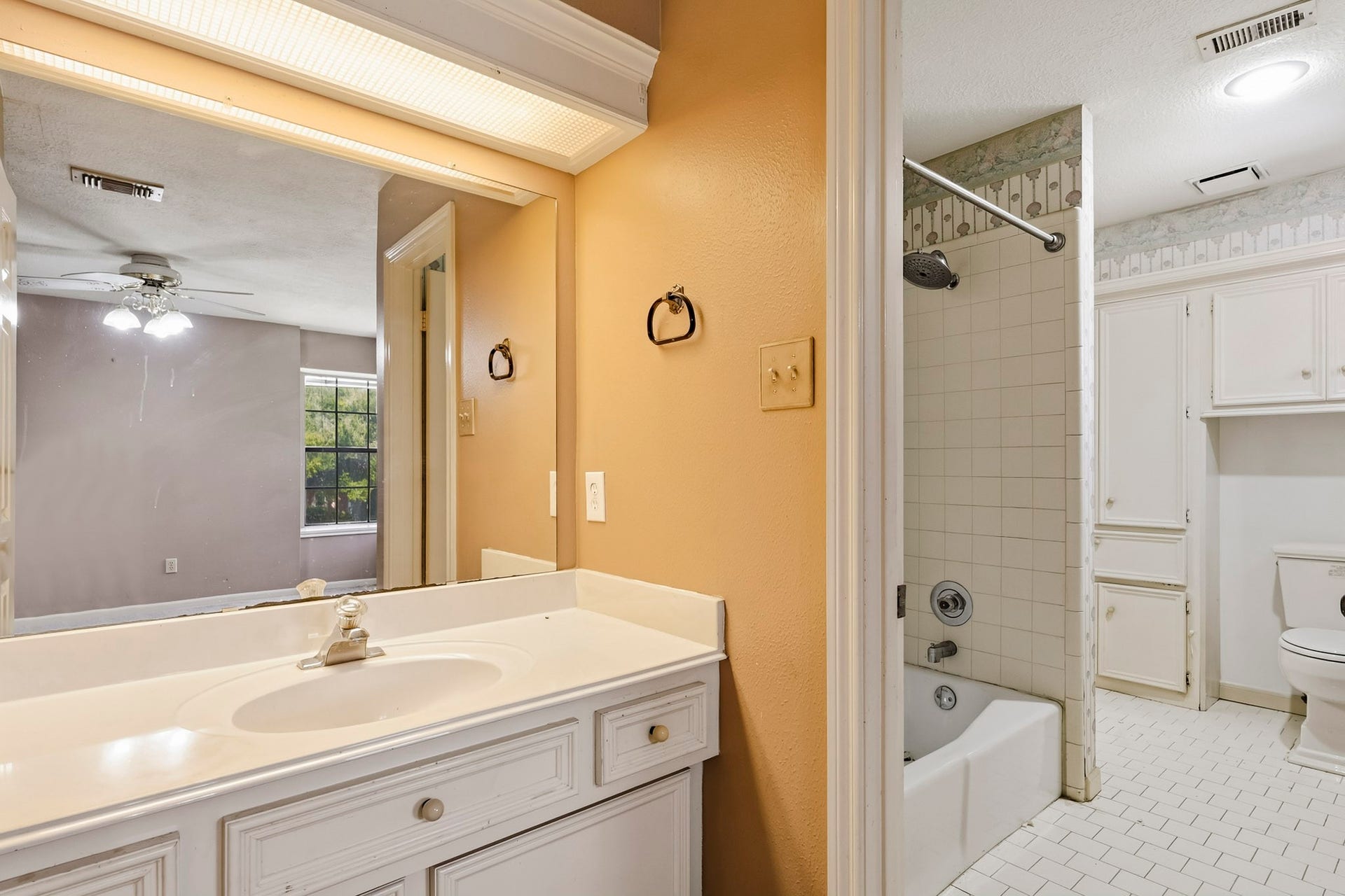 Features a private adjacent bath space equipped with a tiled bathtub and shower combination, extra linen storage cabinets, and clean tile flooring throughout.