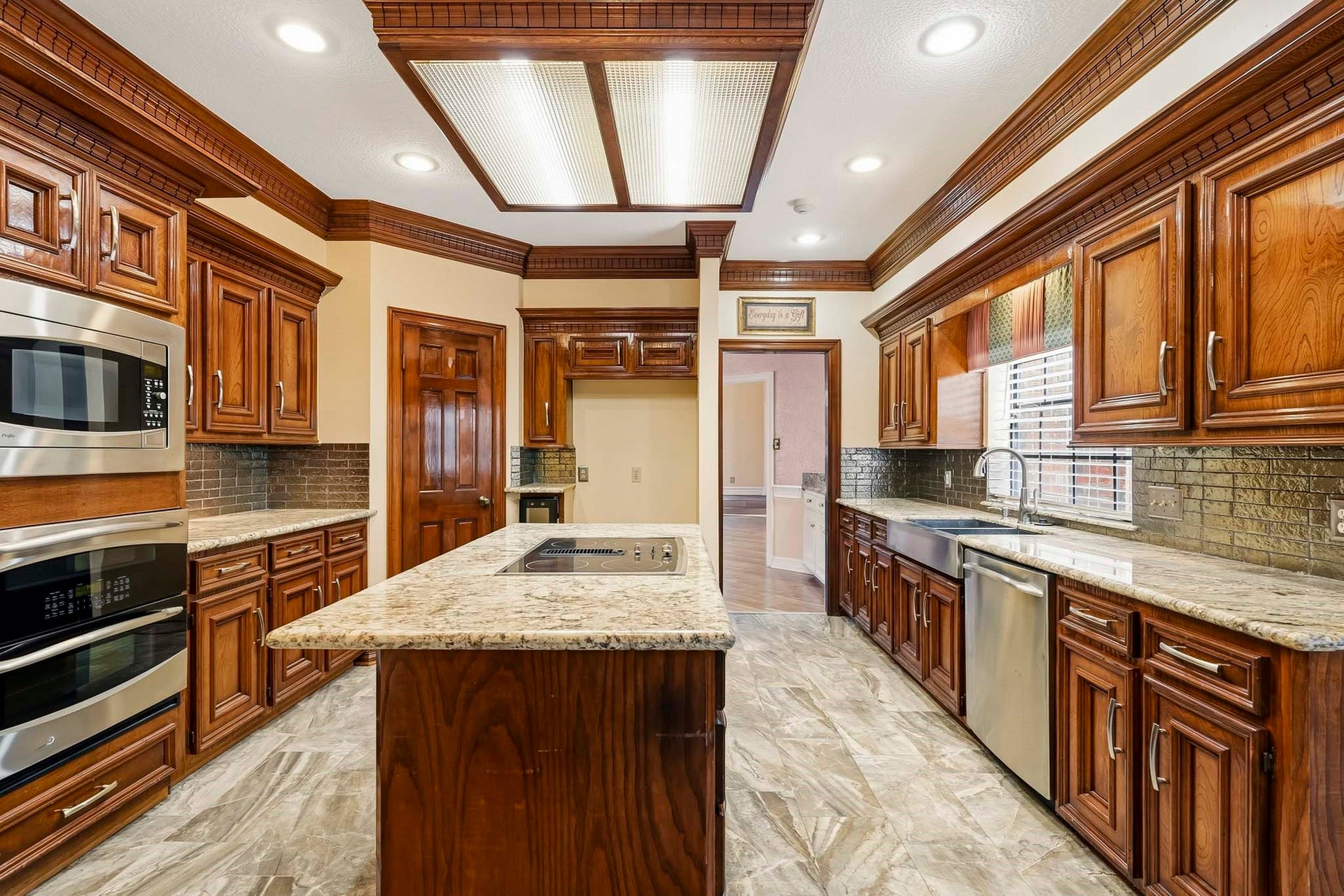 The heart of the home! Highlights a central cooktop island, glistening granite counters, double wall ovens, and custom wood cabinetry crafted for luxurious living.