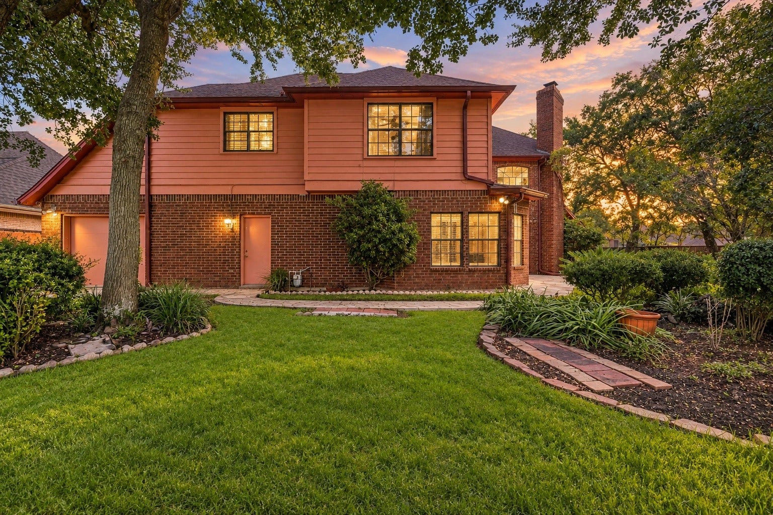Serene backyard sanctuary framed by a canopy of mature shade trees, stone-bordered flower beds, and a lush green lawn.