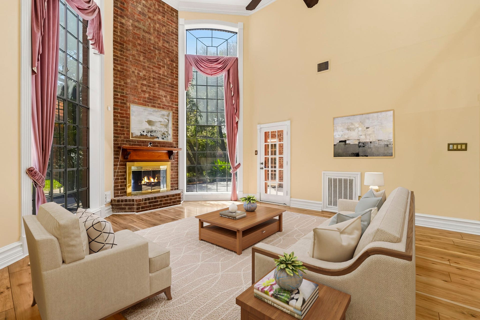 Virtually Staged: Spacious main living room featuring soaring vaulted ceilings and polished hardwood flooring. Anchored by a floor-to-ceiling brick fireplace, the space is flooded with natural light from two tall, arched multi-pane windows.