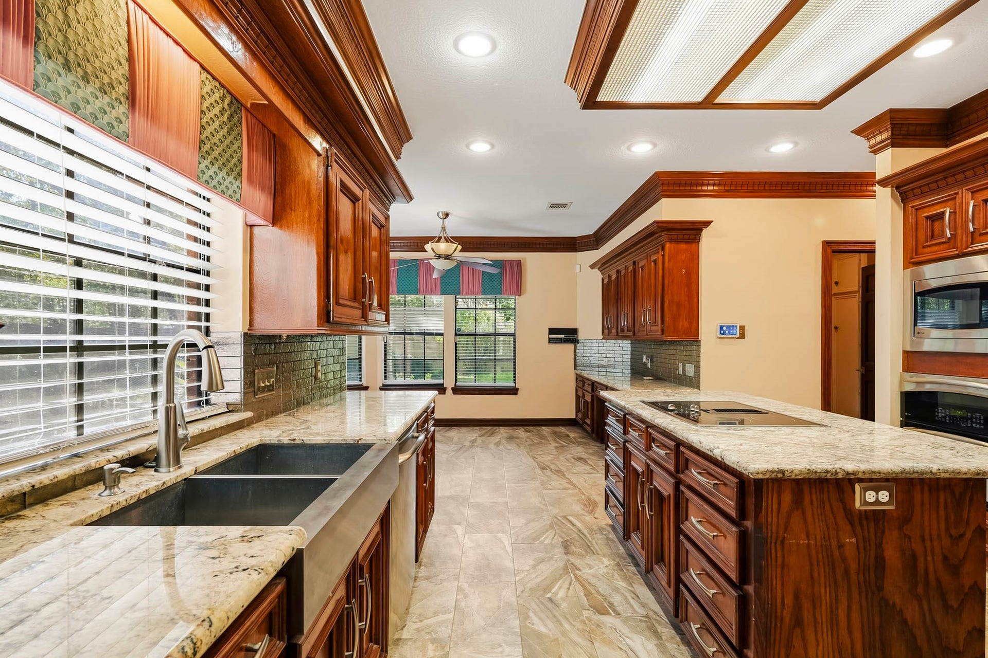 Expansive kitchen equipped with custom wood cabinetry, a center island with cooktop, granite counters, a stainless apron-front sink, and built-in appliances.